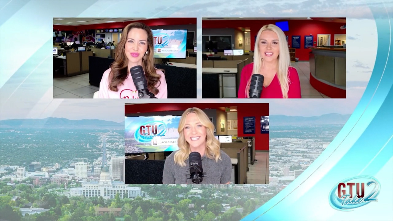 Three women in a news studio, two with microphones, smiling at the camera, with a cityscape background.