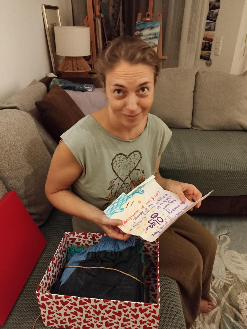 Woman sitting on a couch holding a wrapped gift with a heart drawing on her shirt.