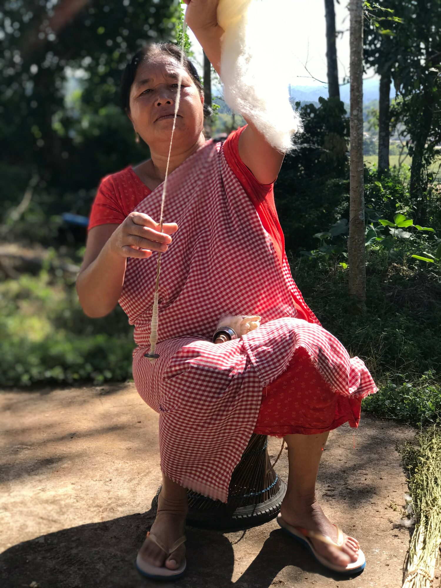 Child sitting outdoors holding a cotton candy stick with a cloudy sky and trees in background.