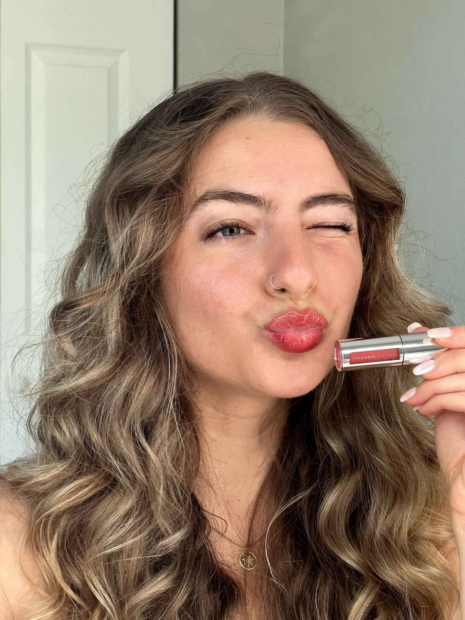 Woman with wavy hair making a kissy face, holding a lipstick near her lips.