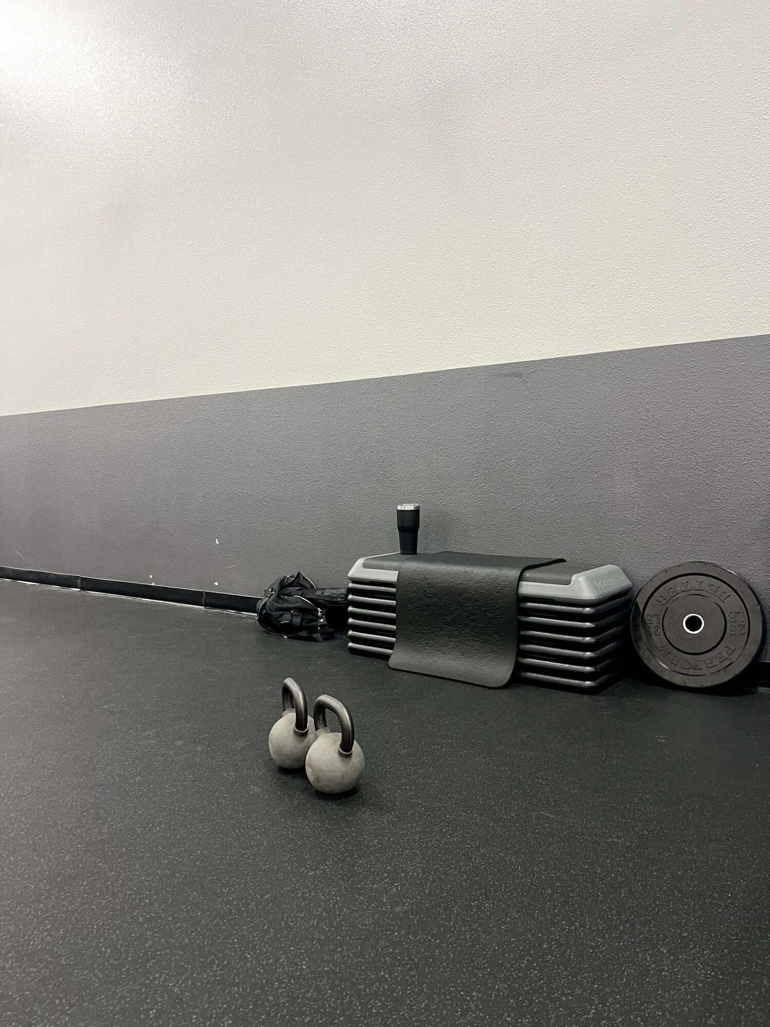 Workout equipment, including a foam roller and a massage ball, on a black floor with a gray wall background.
