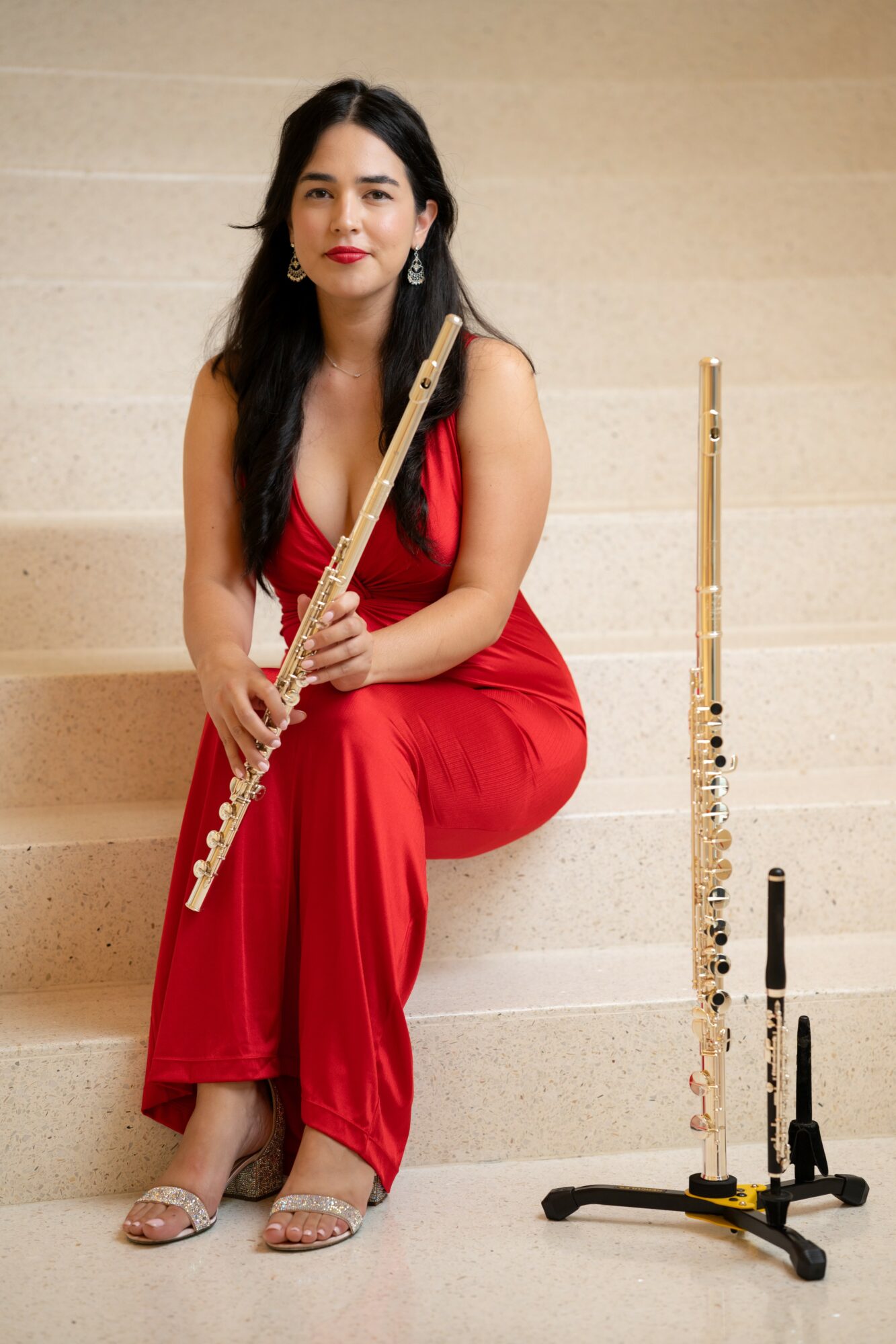 Woman in red dress sitting on stairs holding a flute, with another flute on a stand beside her.