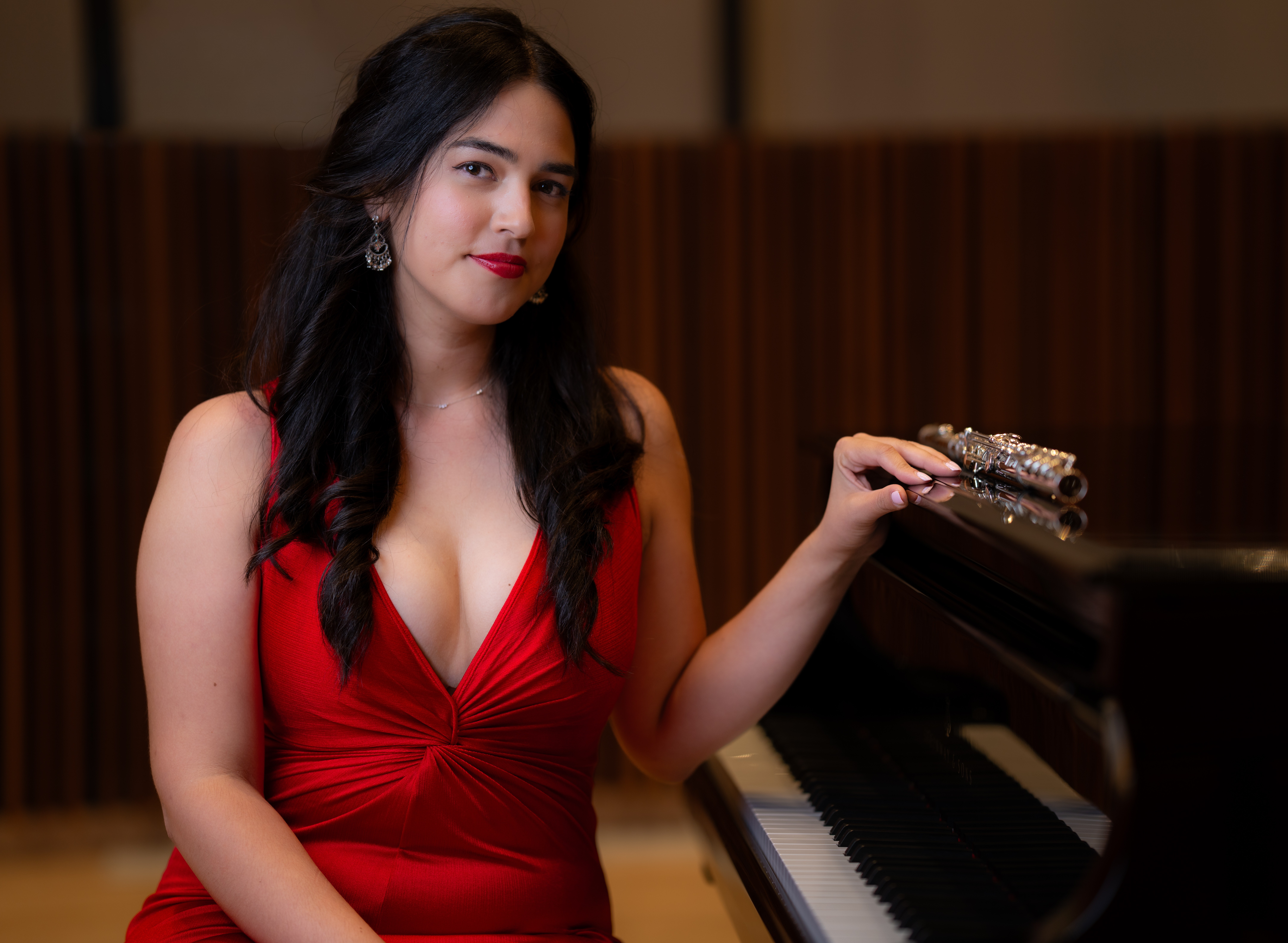 Woman in red dress sitting at a piano, holding a small clutch, with a wooden background.