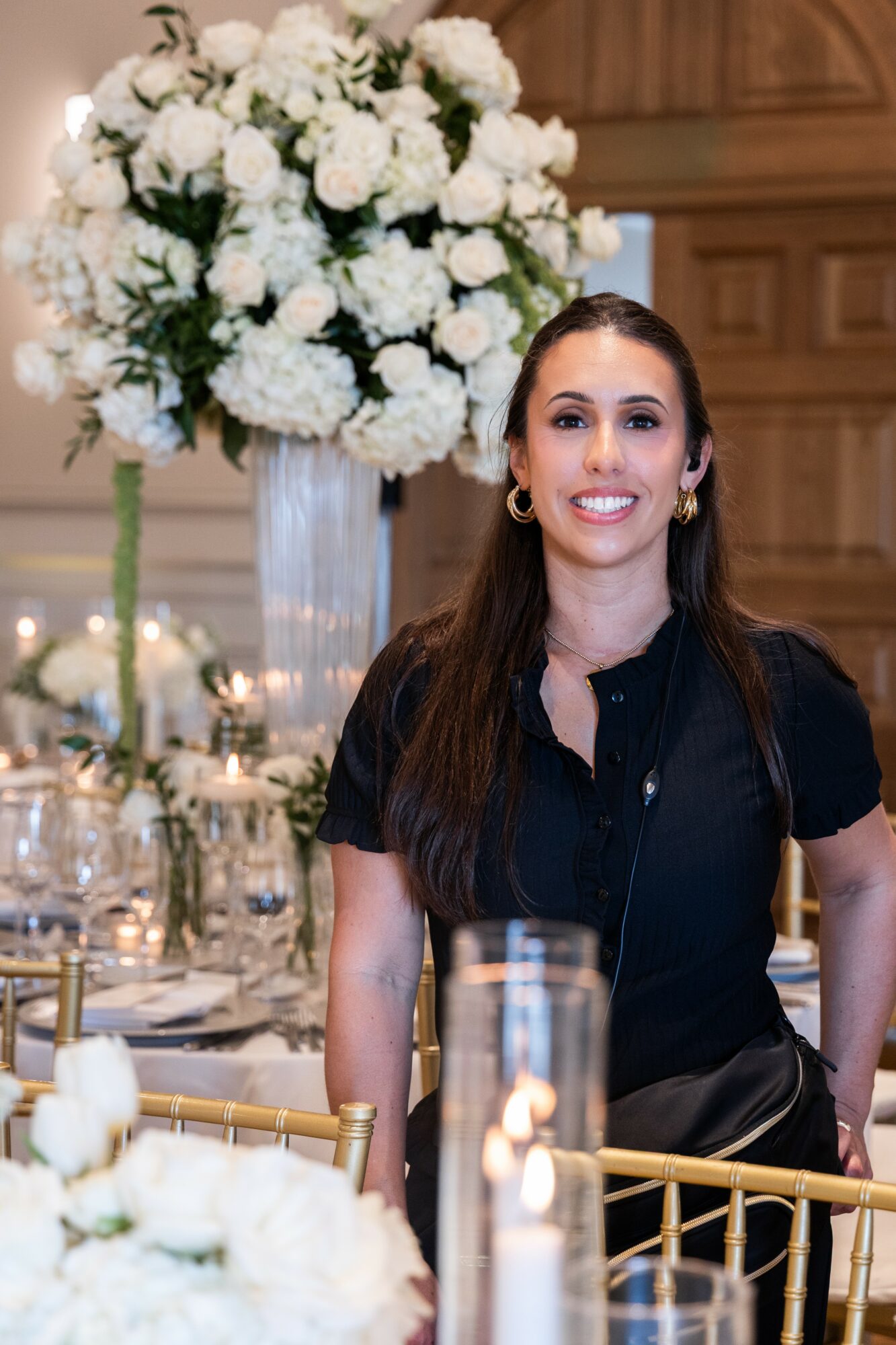 Young woman with long dark hair smiling at a decorated event table with white flowers and candles.
