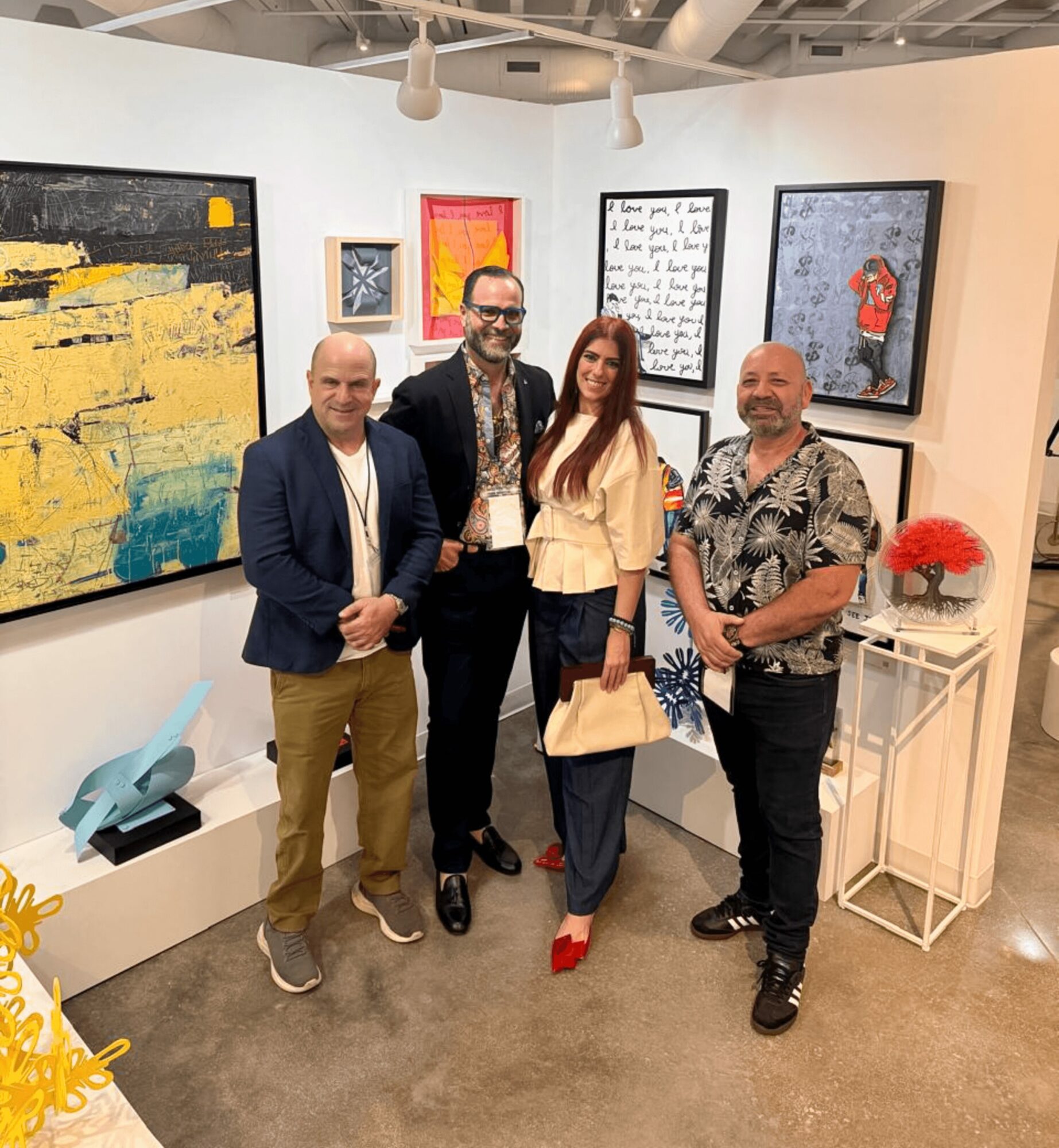 Four people stand in an art gallery with colorful paintings on the wall behind them. They pose for a photo.