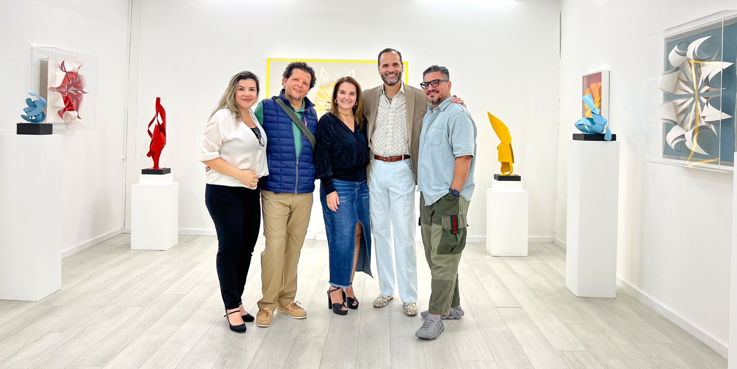 Group of five people standing in an art gallery with sculptures and paintings on white walls.