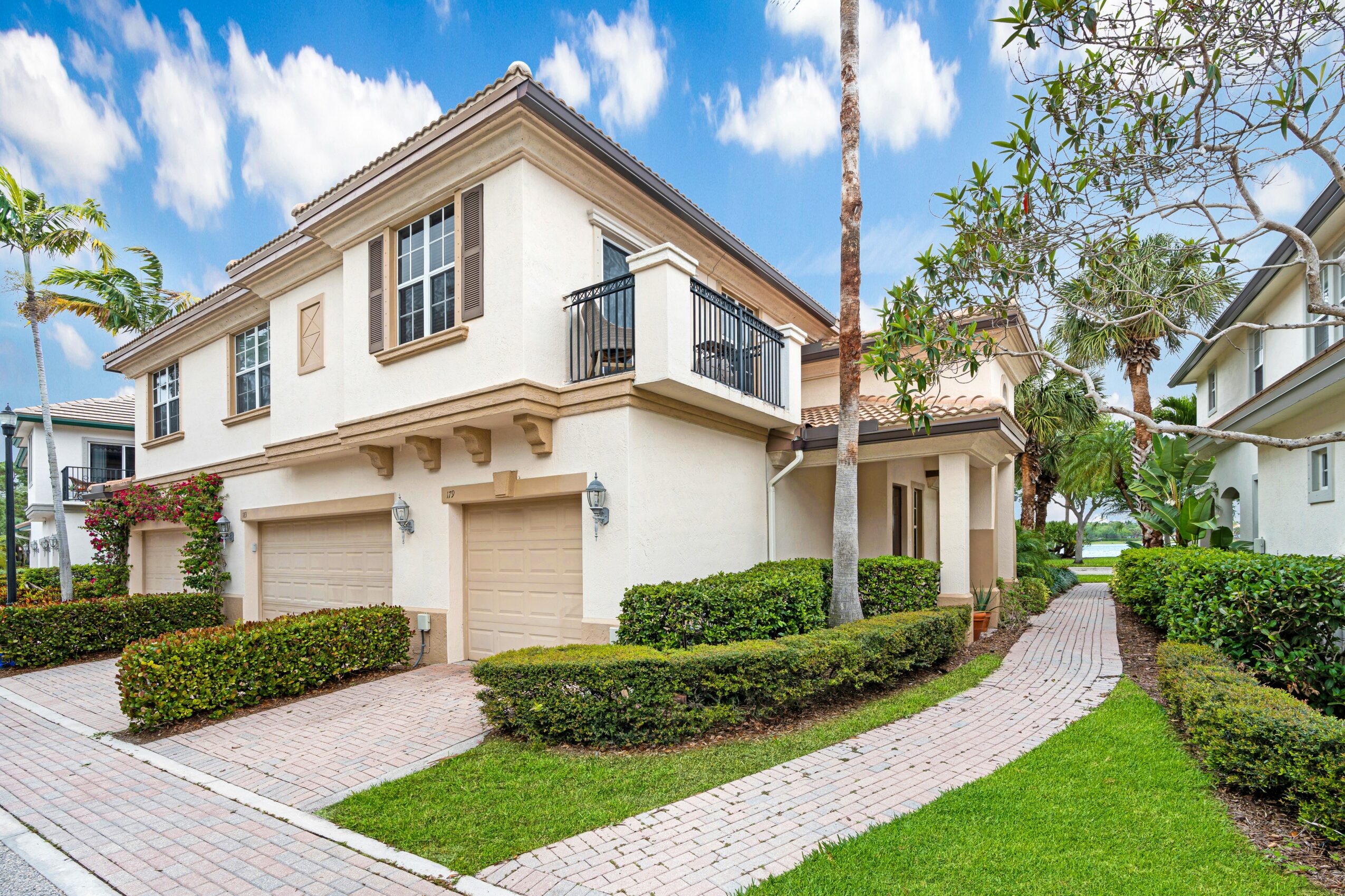 Two-story house with white exterior, garage doors, and a curved brick pathway surrounded by green bushes and trees.