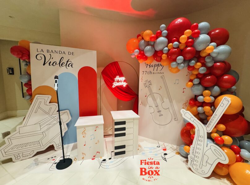Balloon arch with red, orange, gray, and white balloons, musical instrument cutouts, and a sign for a music-themed celebration.