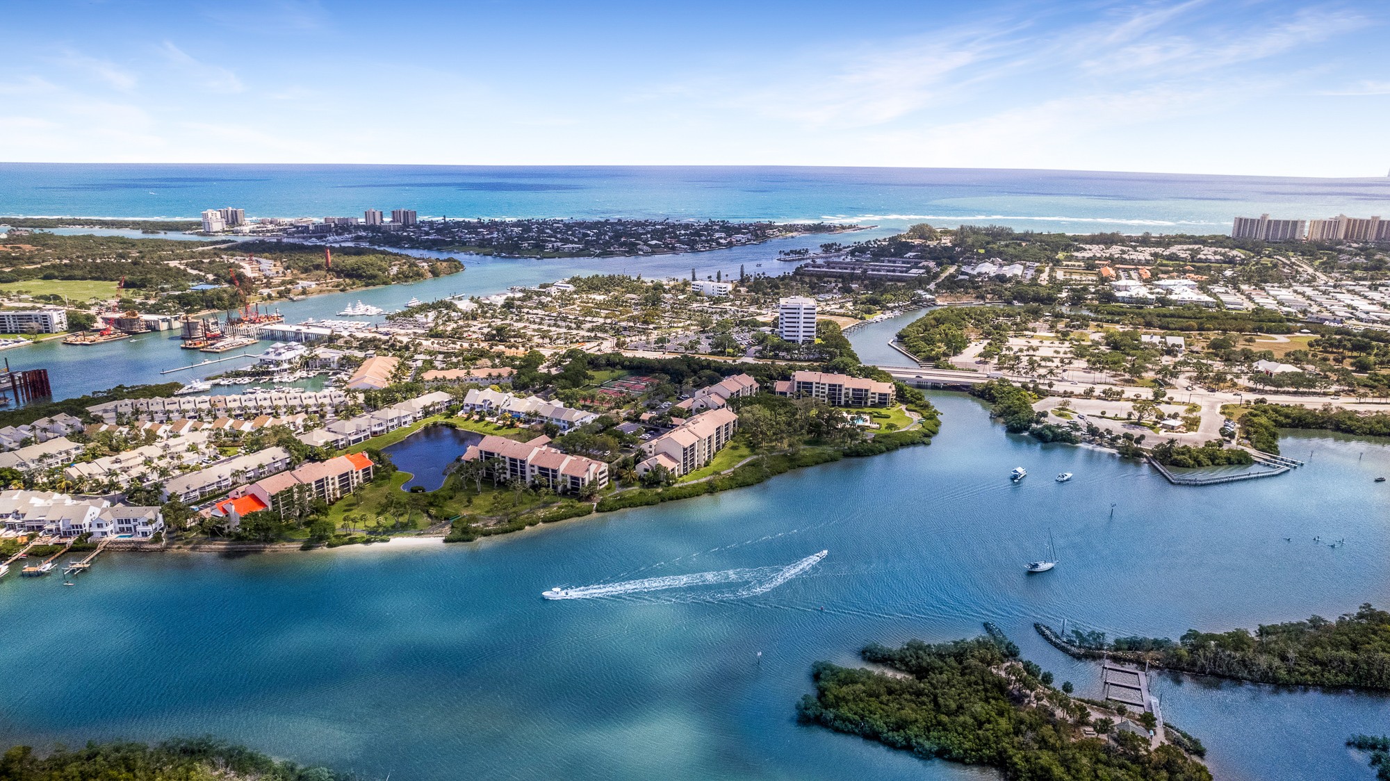 Aerial view of a coastal city with water bodies, buildings, and a shoreline under a blue sky.
