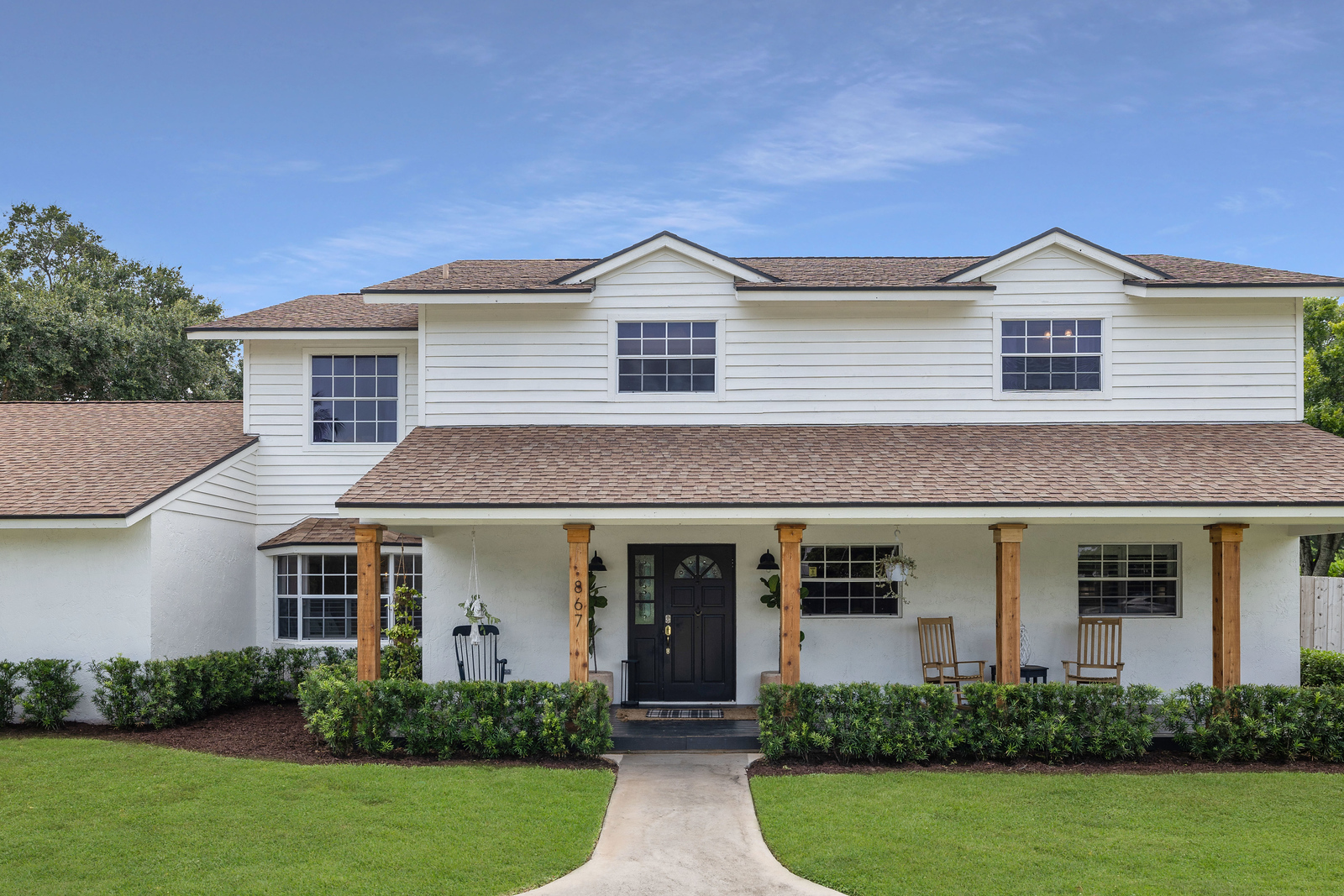 Front view of a two-story house with a porch, black door, white siding, and a well-maintained lawn.