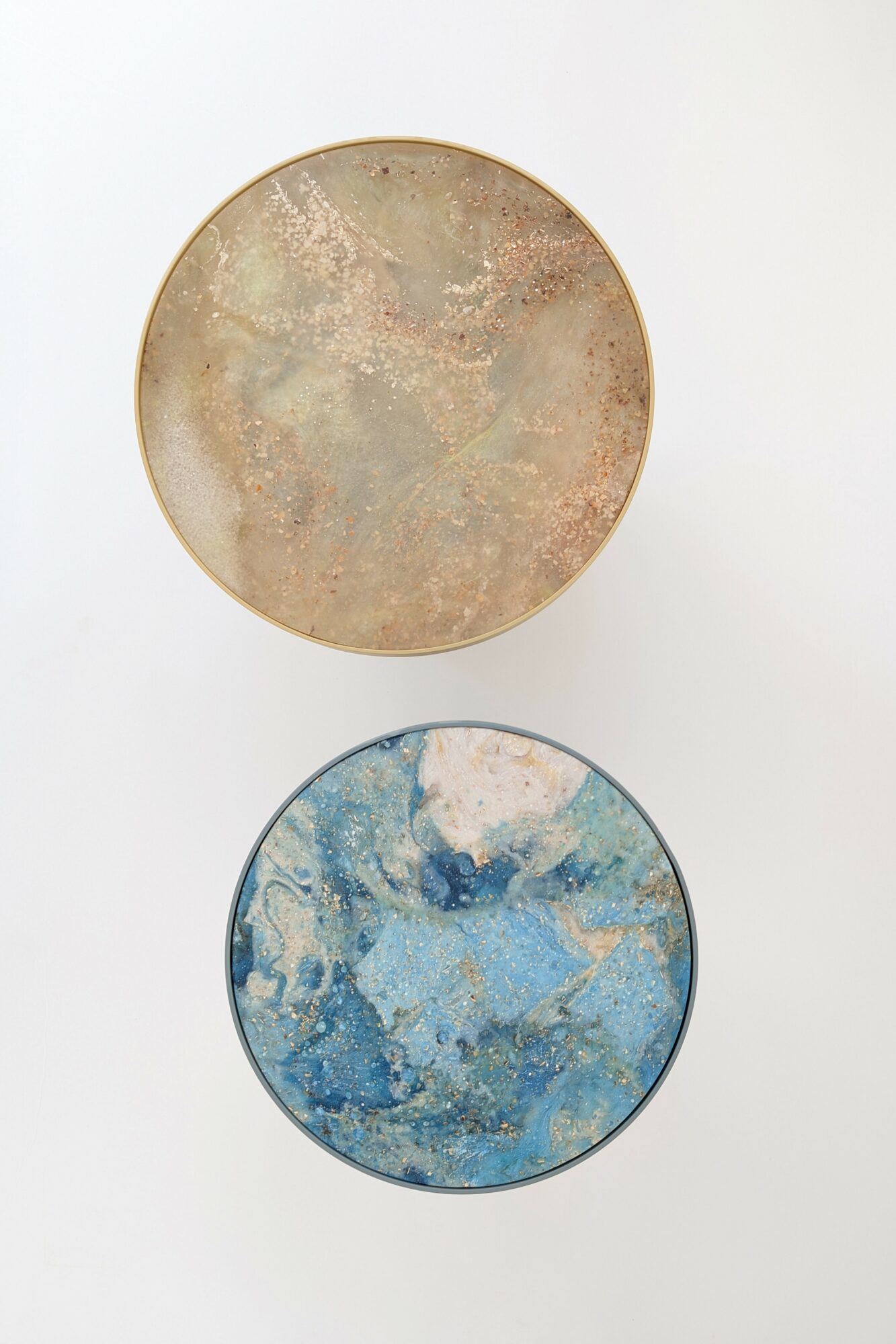 Two round, textured objects with abstract patterns, one in beige and gold tones, the other in blue and white tones, on a white background.