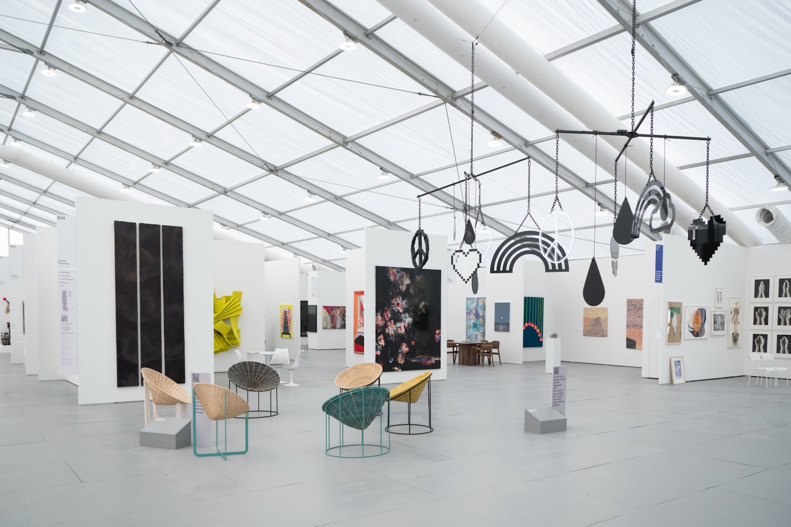Art gallery with white walls, various artworks, and seating areas inside a glass ceiling structure.
