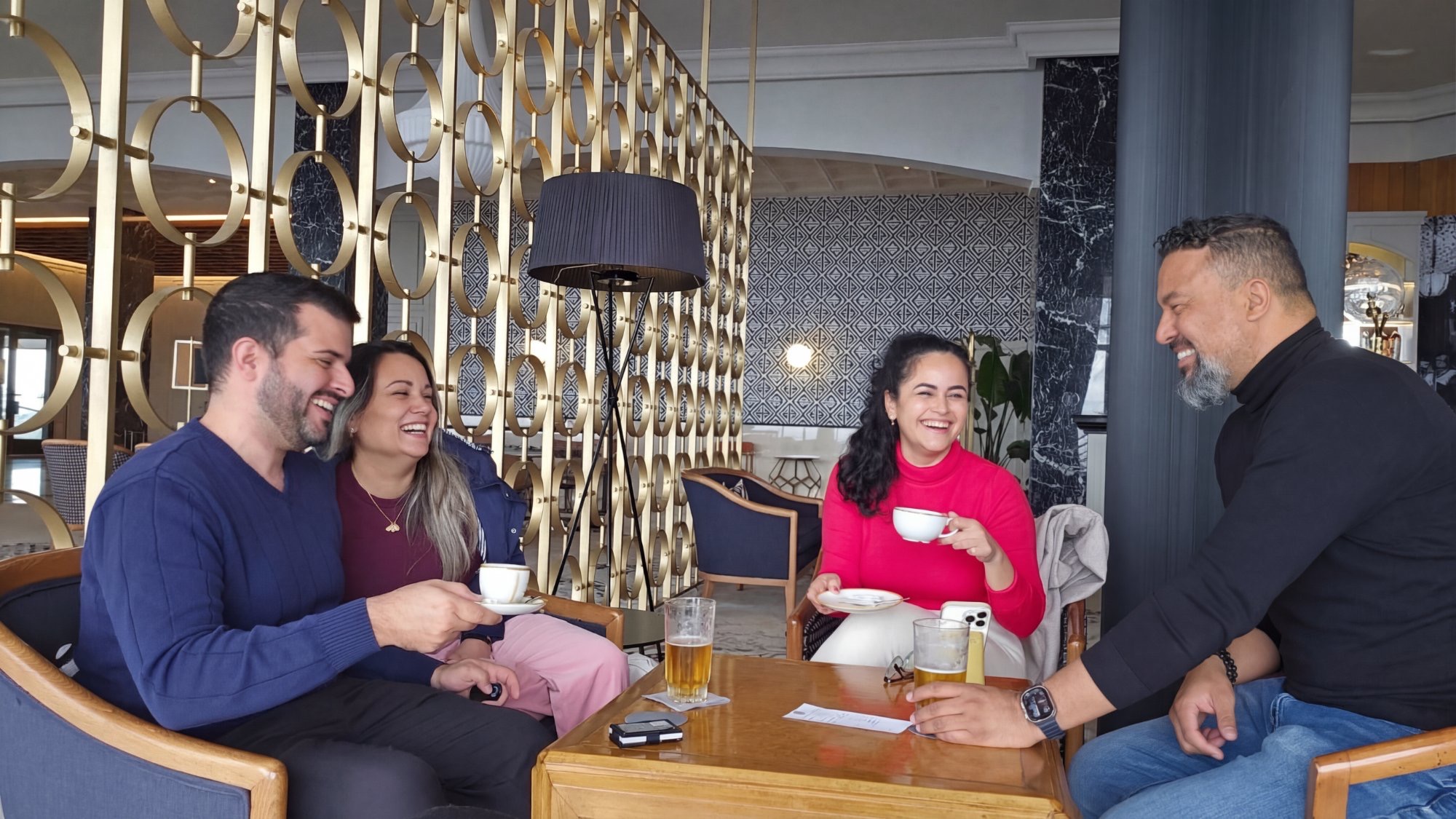 Four people sitting at a table in a modern restaurant, smiling and talking, with drinks and a phone on the table.