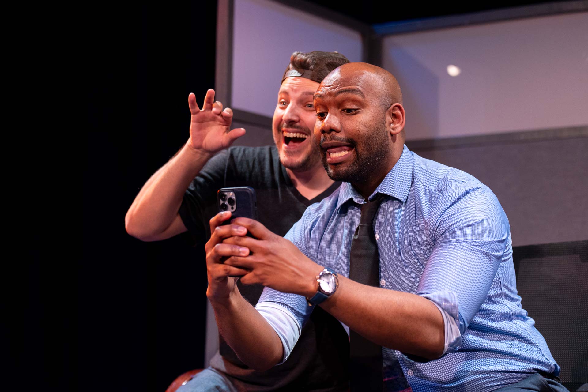 Two men taking a selfie, one smiling and the other making a playful gesture with hand near face.