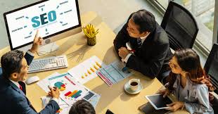 Four people in a business meeting around a table with charts, a computer, and a coffee cup.