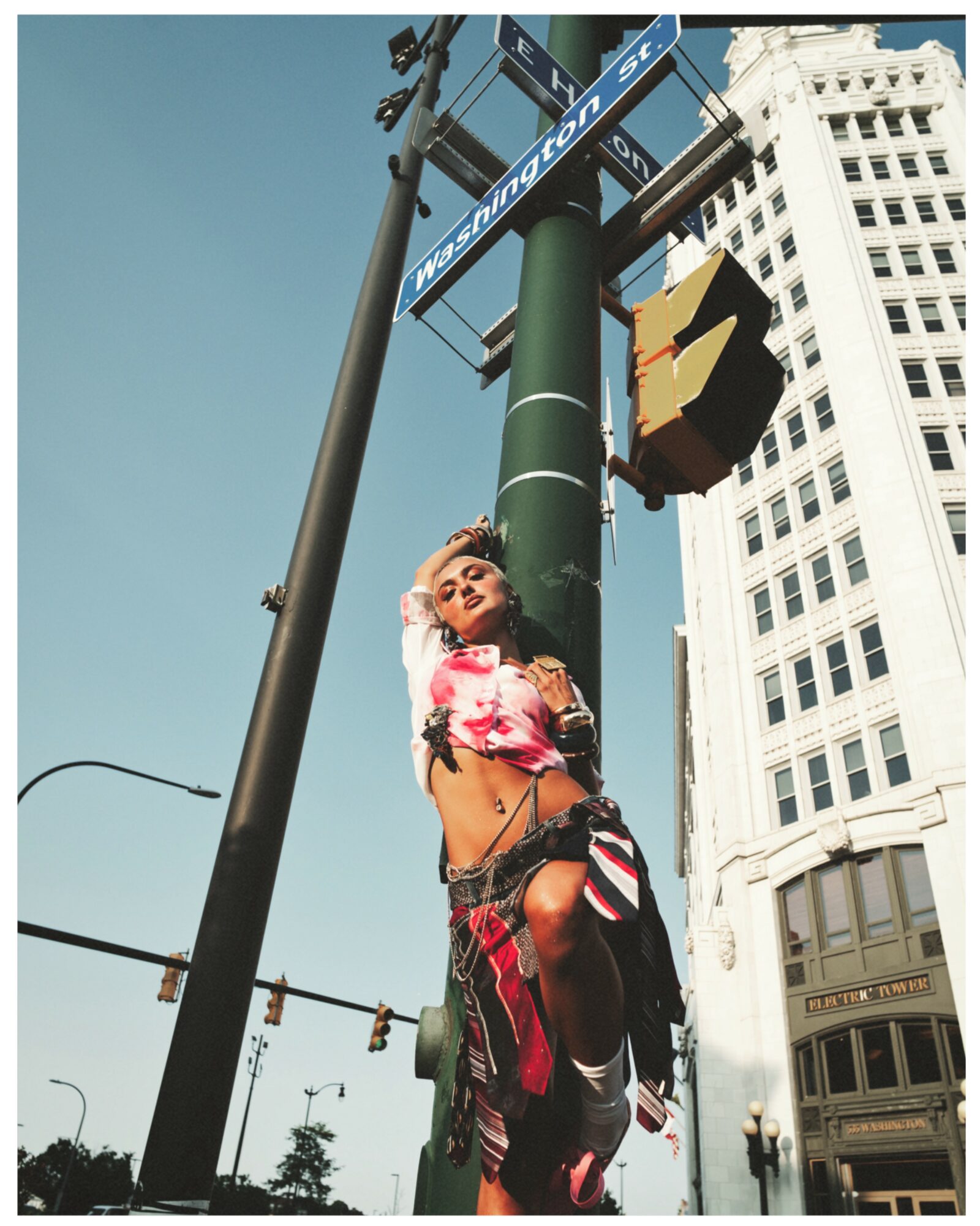 Young woman with floral top and ripped jeans leaning against a street sign pole in an urban setting.