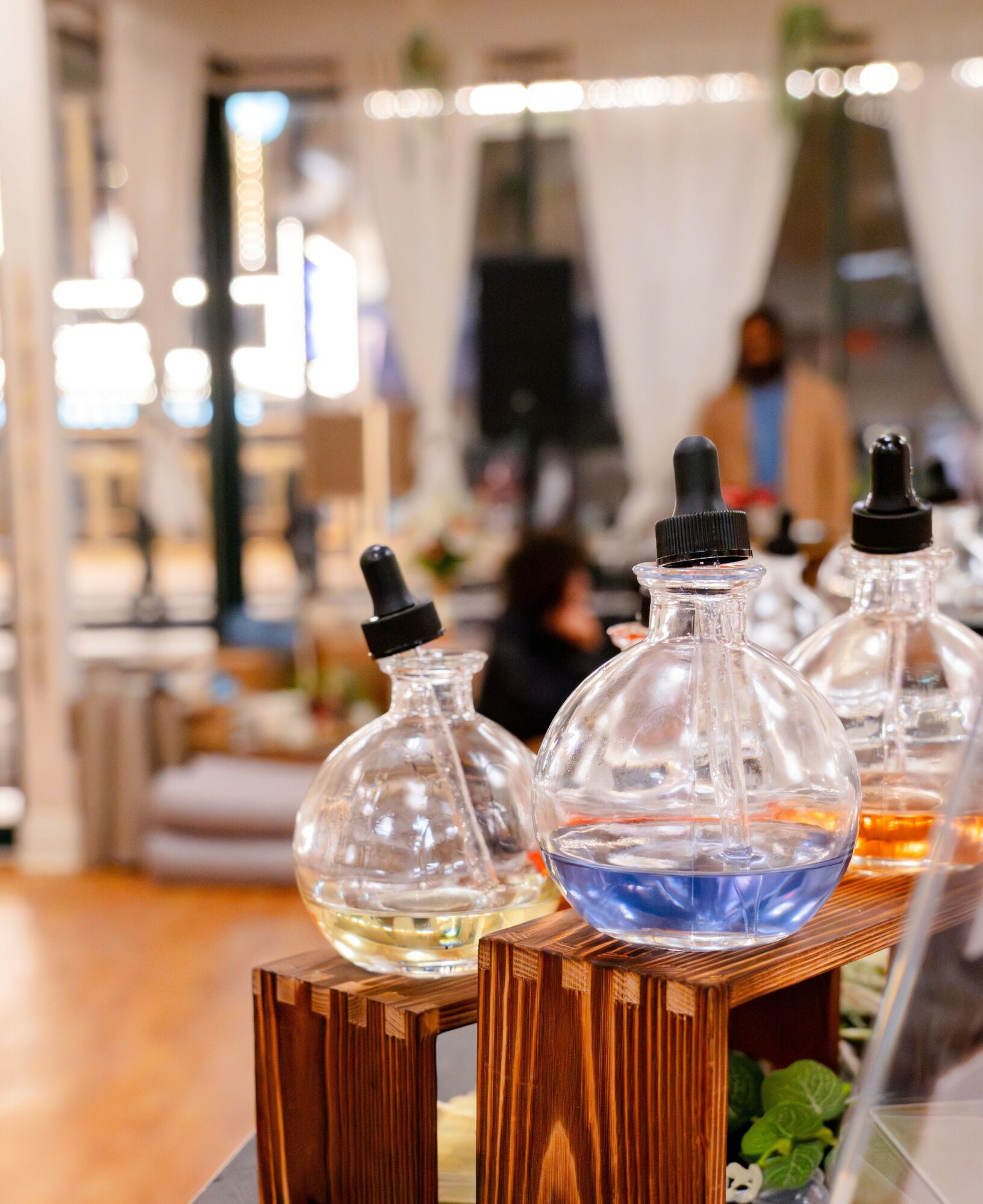 Three glass bottles with droppers on a wooden surface, filled with colorful liquids, in a bright indoor setting.