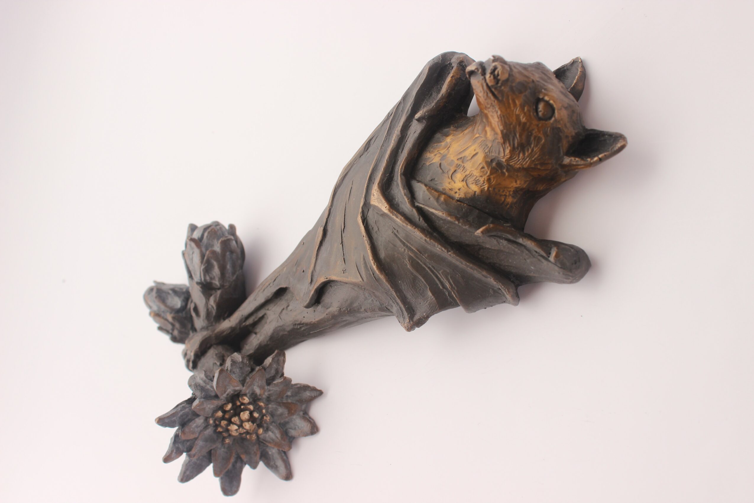 Wooden sculpture of a bear with a fish in its mouth, mounted on a white background.