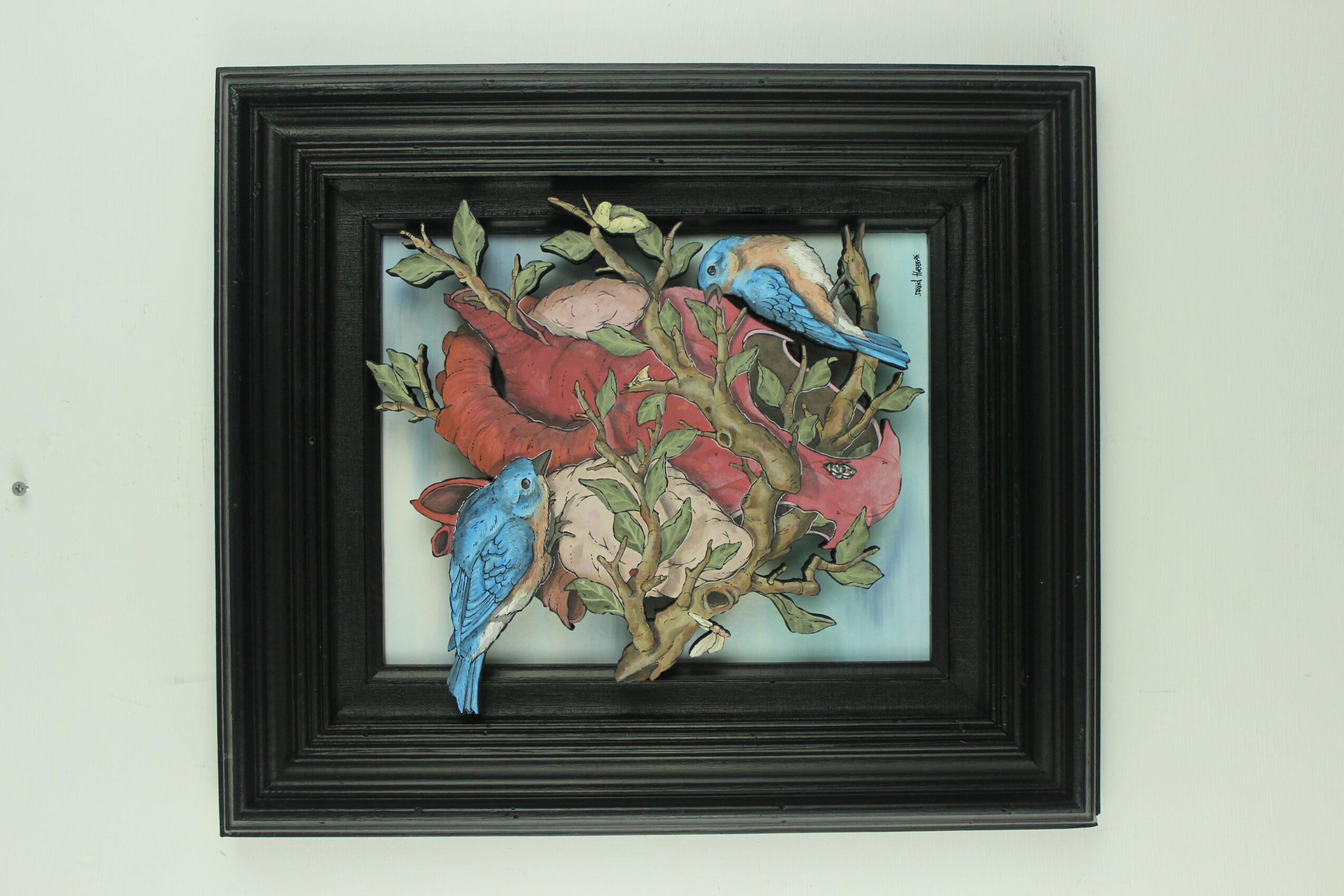 Framed artwork featuring colorful birds and a plant against a light background.