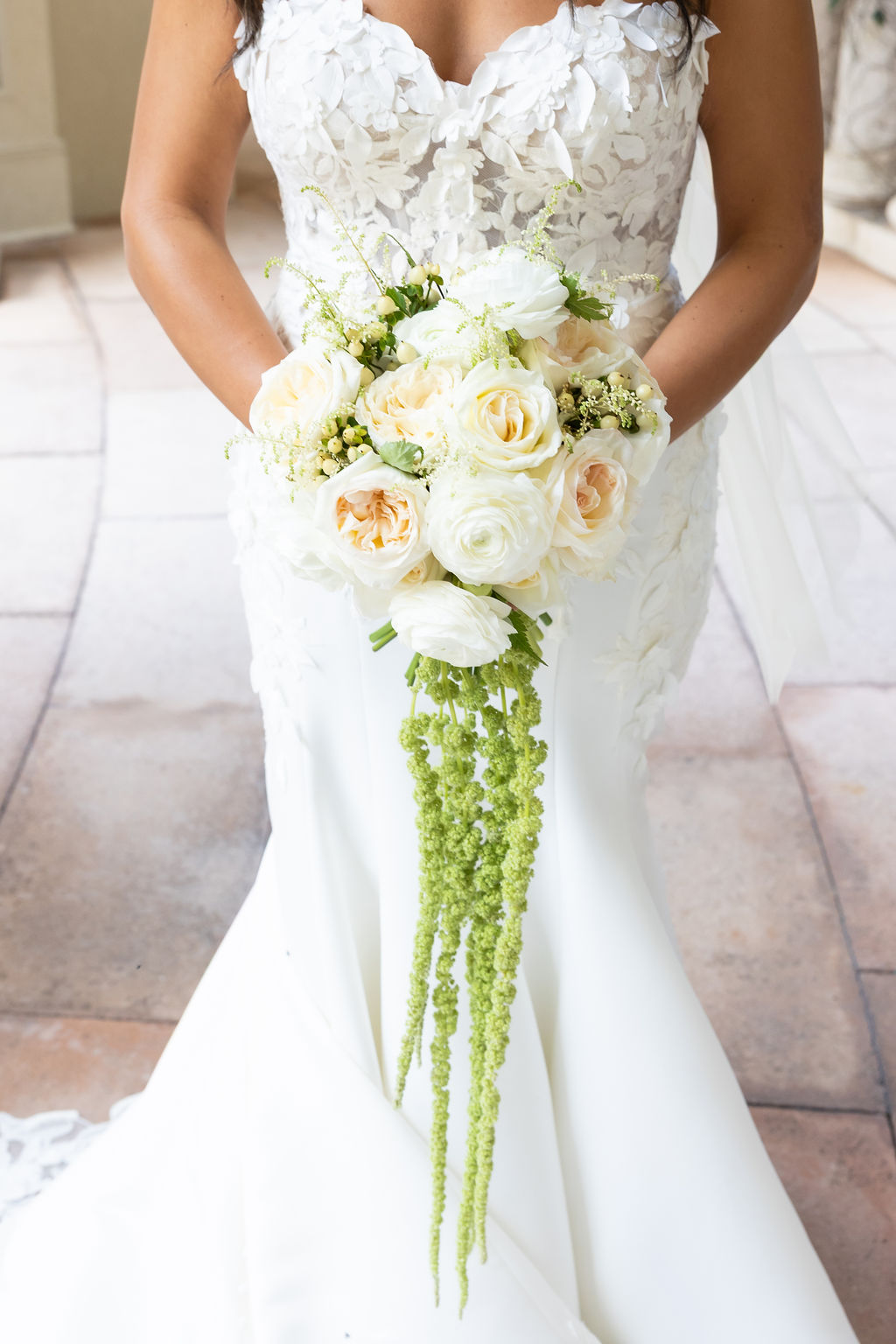 Bride in wedding dress holding a cascading bouquet of white and peach flowers with green accents.