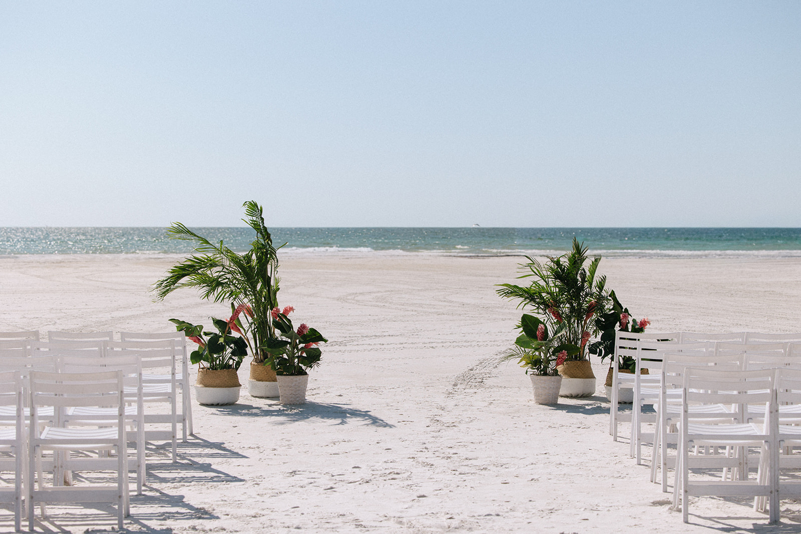 Beach scene with chairs and potted plants facing the ocean under a clear sky.