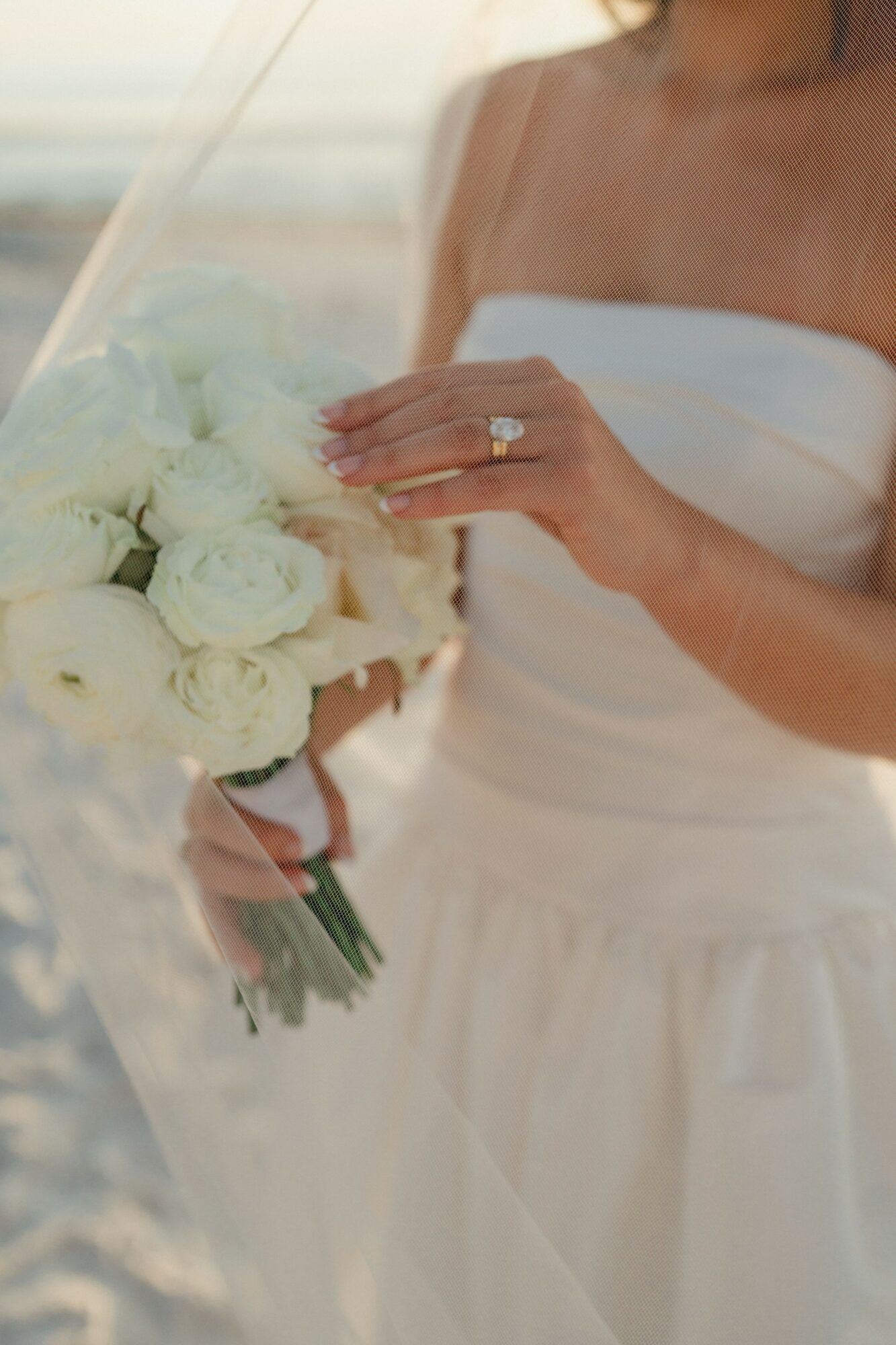 Close-up of a woman in a strapless white dress holding a bouquet of white roses, showing her hand with a ring.