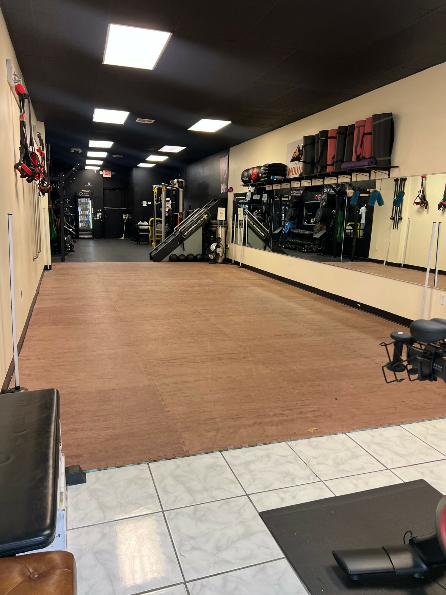 Empty fitness studio with wooden floor, mirrors, and workout equipment on shelves and racks along the walls.