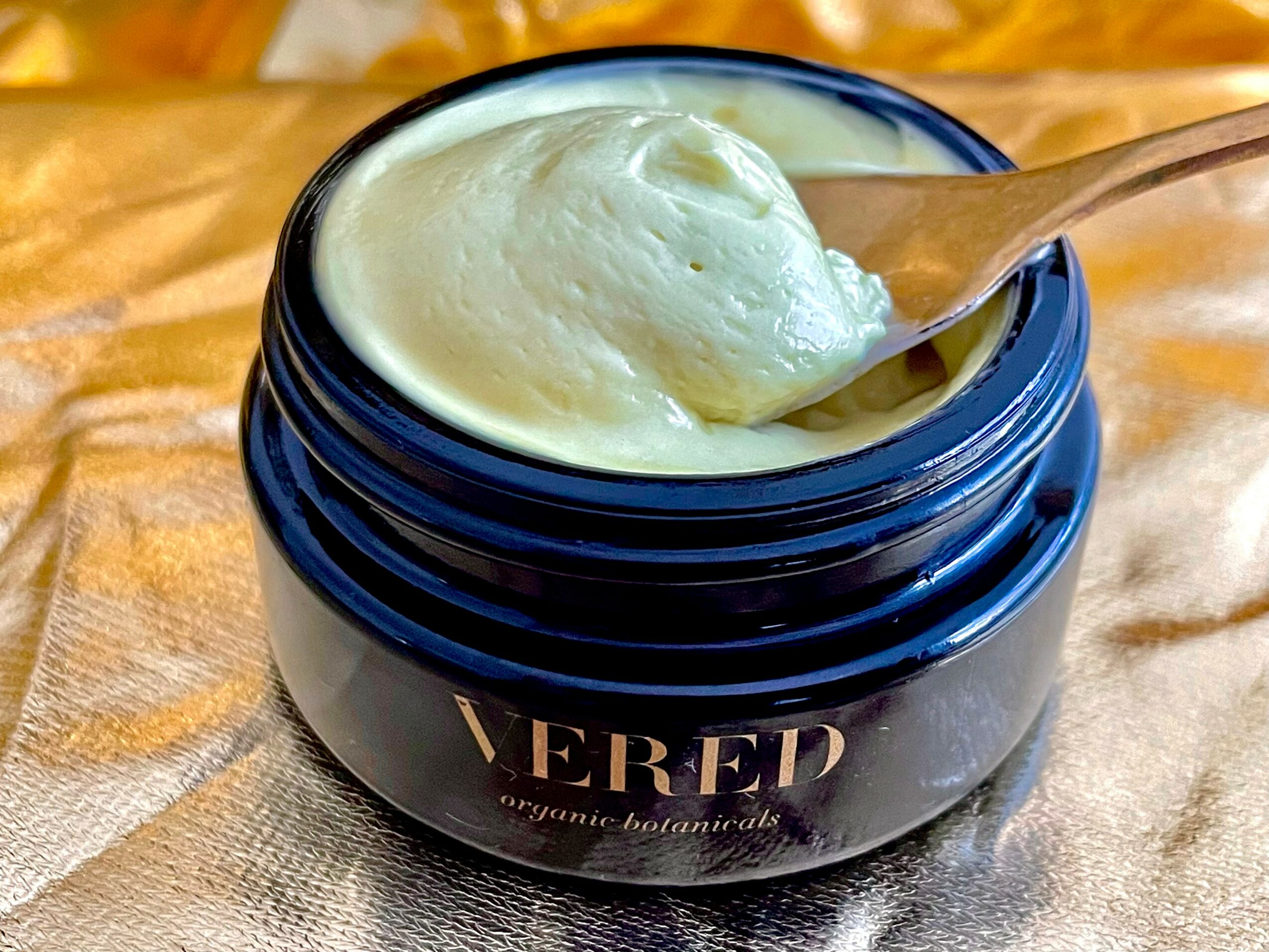 Open jar of creamy substance with a spoon inside, placed on a fabric surface.