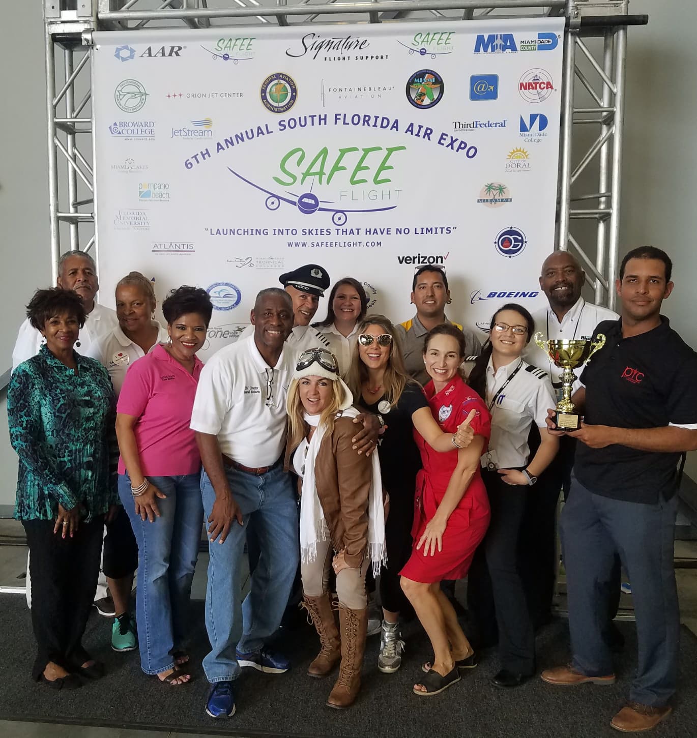 Group of people posing in front of a banner at the South Florida Air Expo, some holding a trophy.