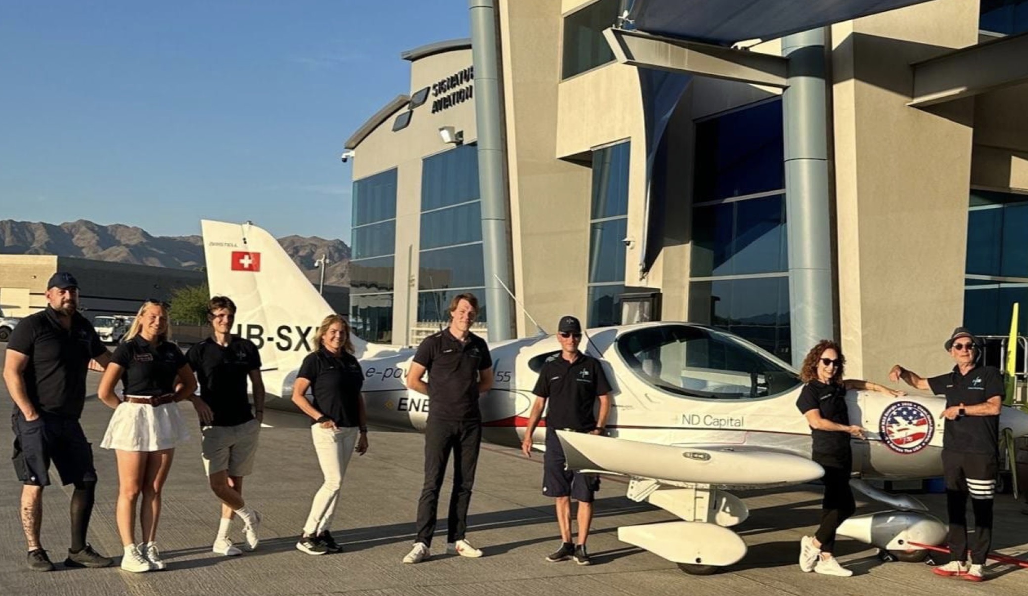 Group of people standing in front of a modern building and a small aircraft outdoors.