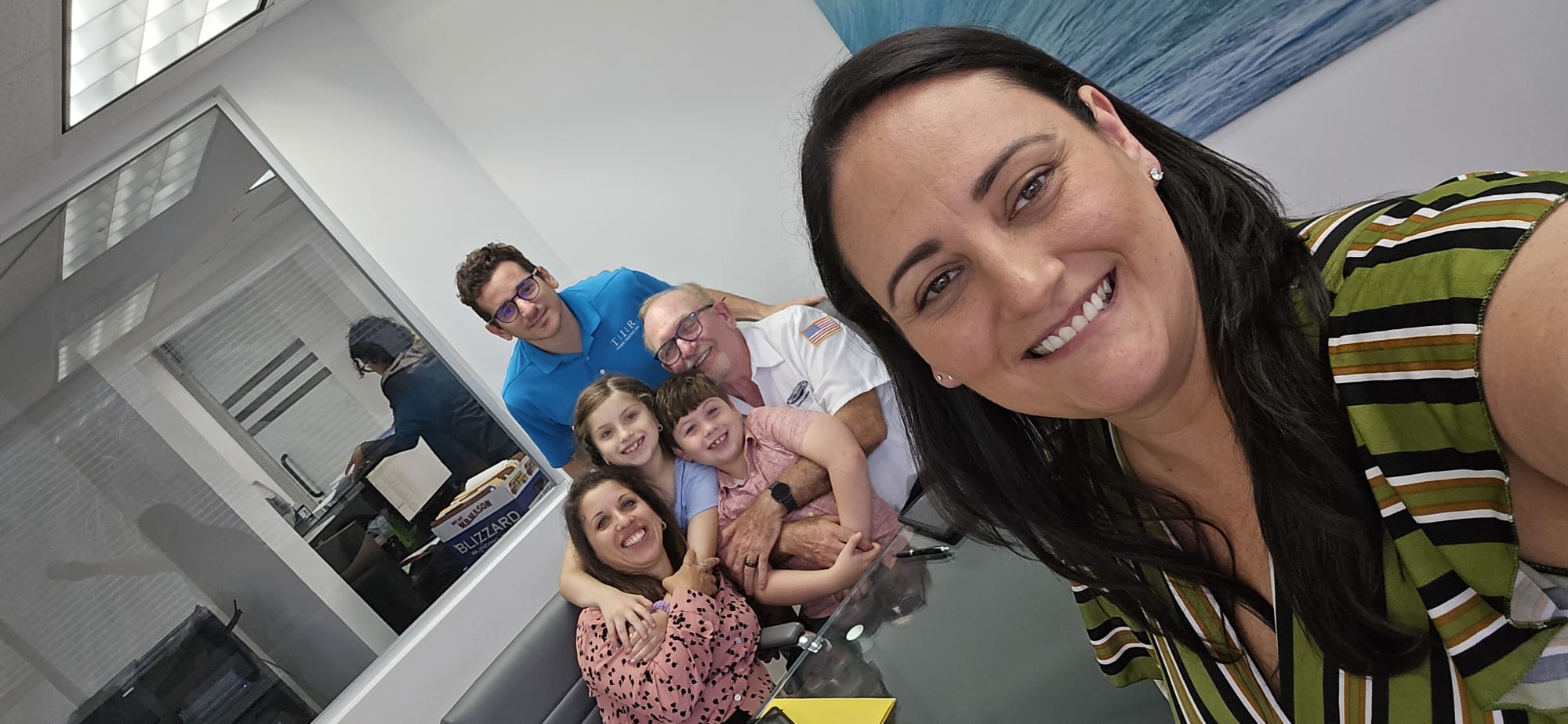 Group of five people, including children, smiling and taking a selfie in a room with a glass window.
