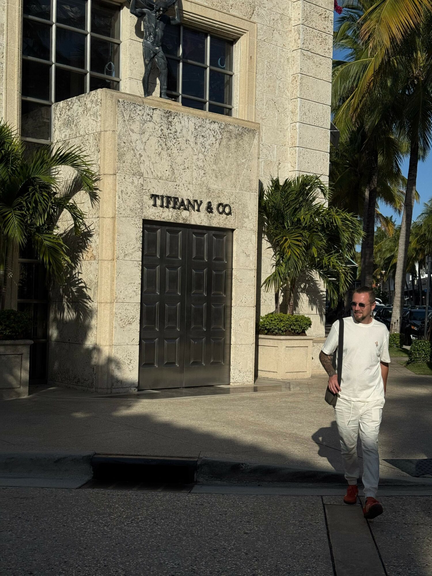 Person walking past Tiffany & Co. store with palm trees and building facade in background.