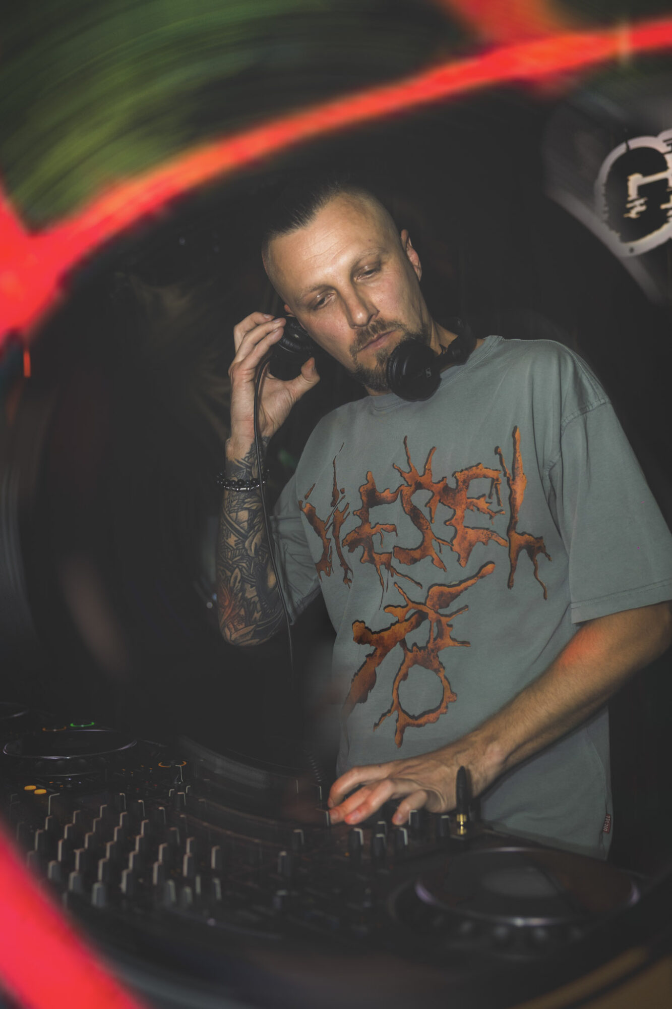 DJ with headphones adjusting equipment in a dark environment with colorful light streaks.