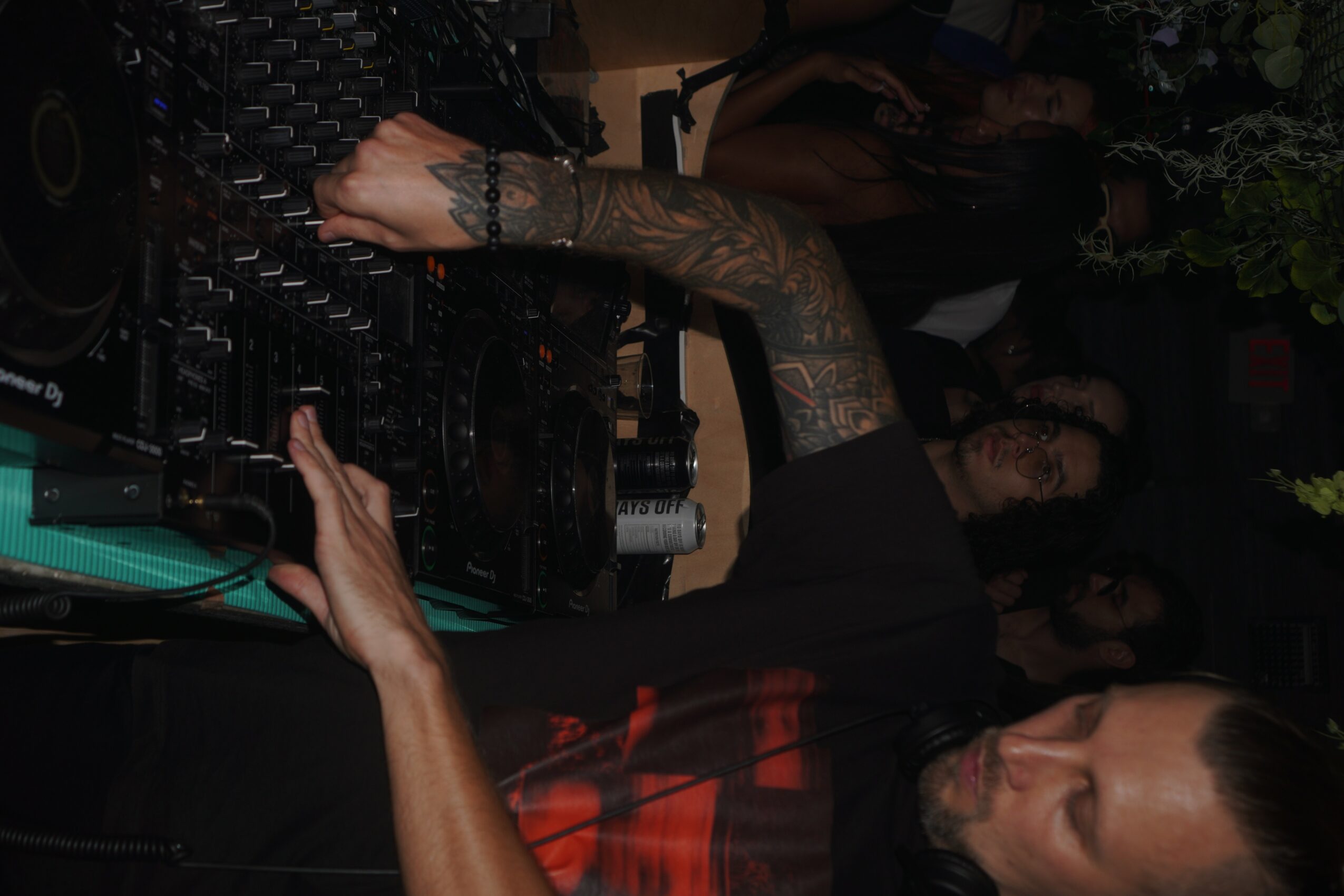 Person with tattooed arm operating DJ equipment in a dark setting.