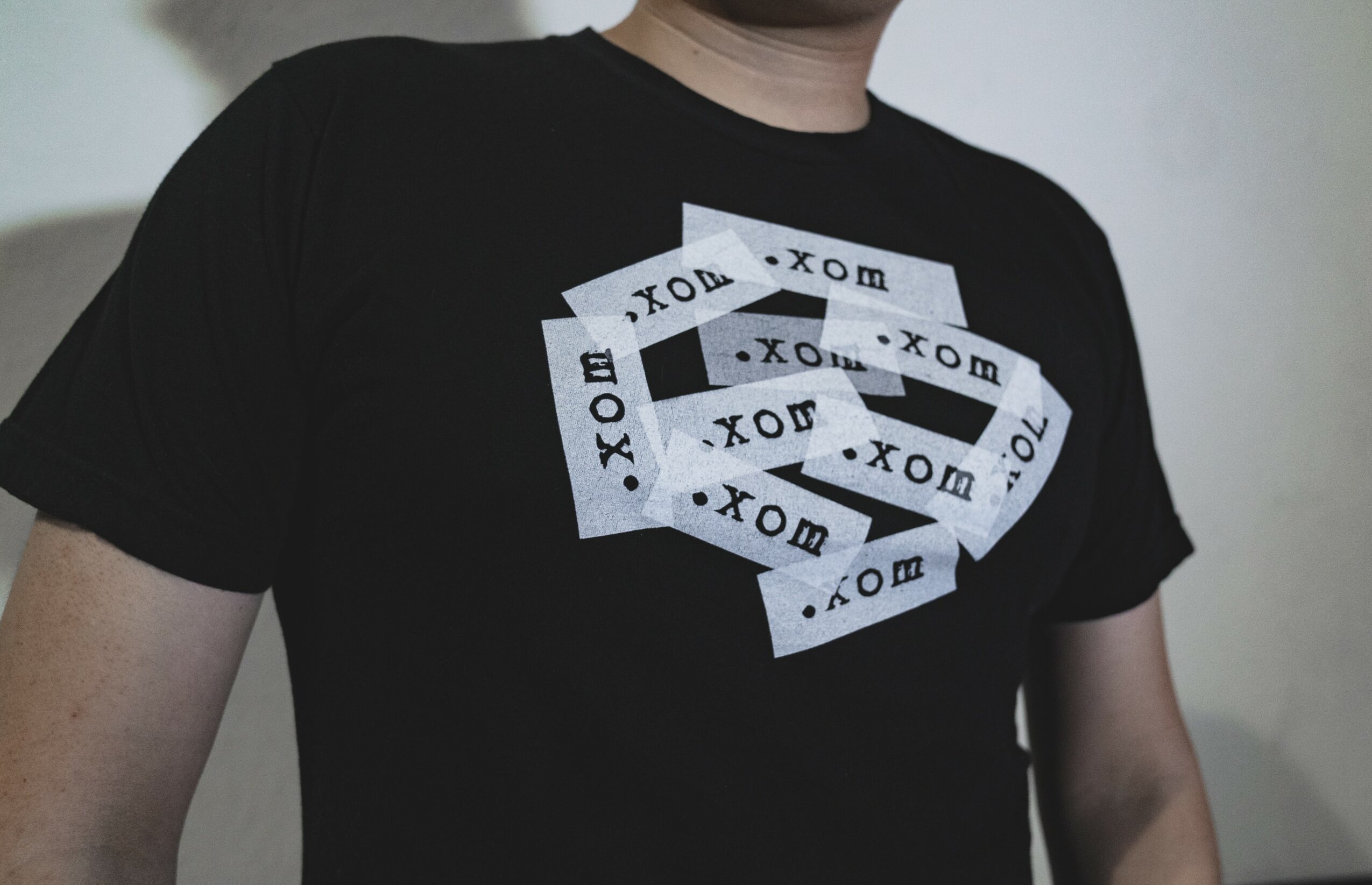 Person wearing a black T-shirt with multiple overlapping XOX and .com patterns on the front.