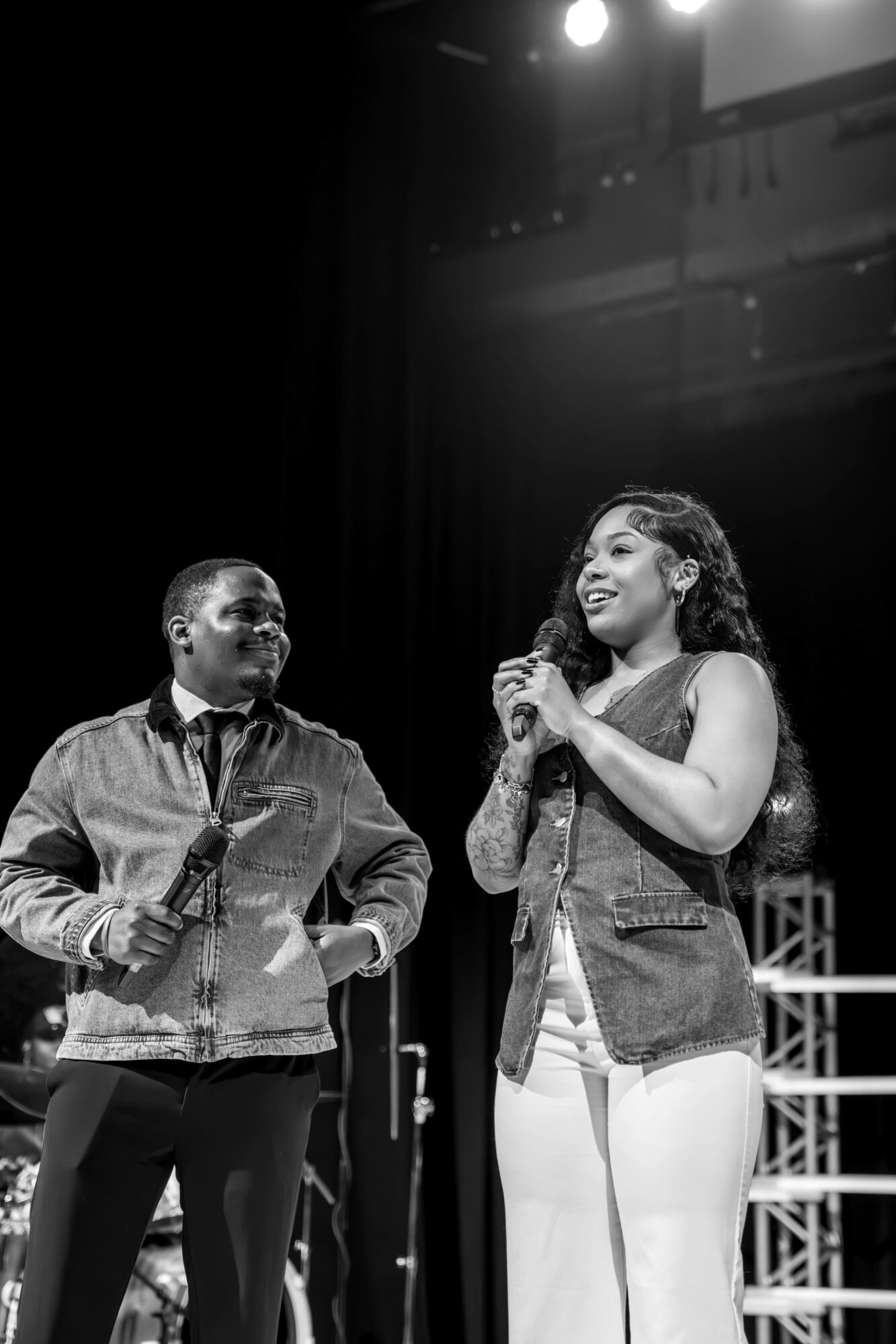 Two women on stage, one holding a microphone, smiling and engaging with each other.