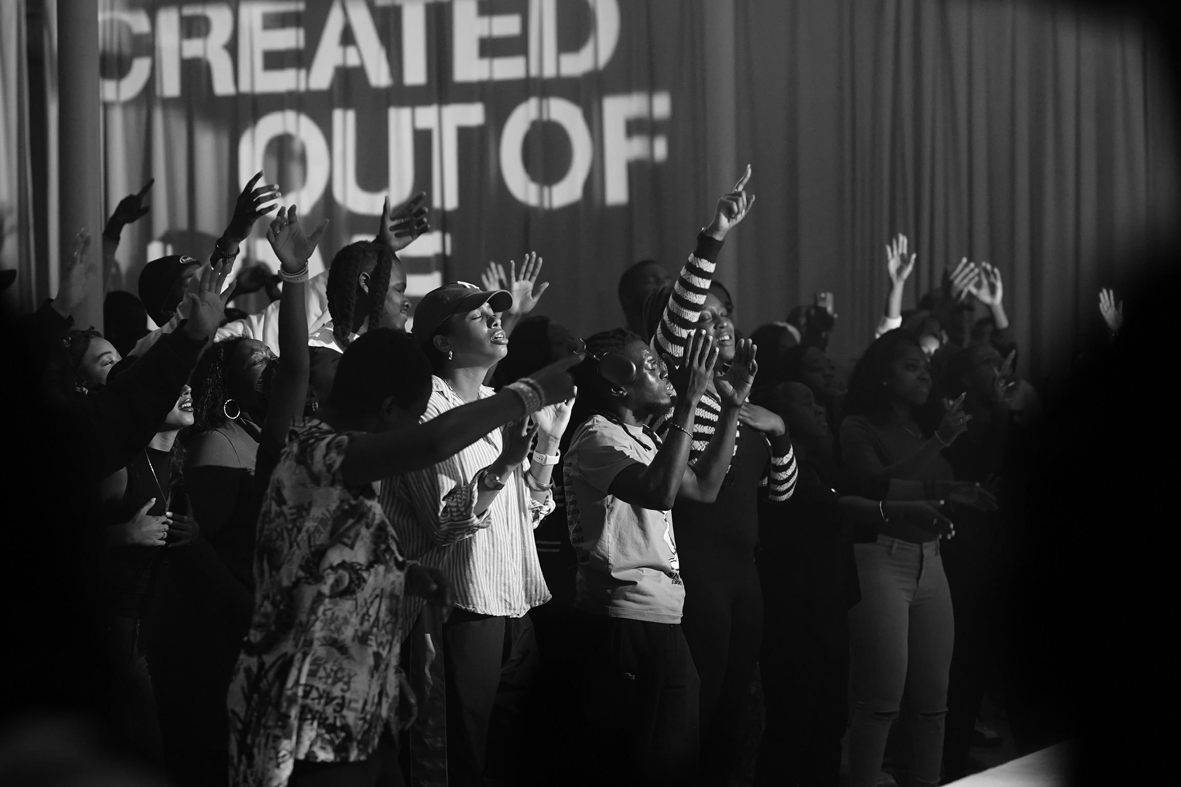 Group of people on stage raising hands during an event, with a large screen in the background displaying partially visible text.