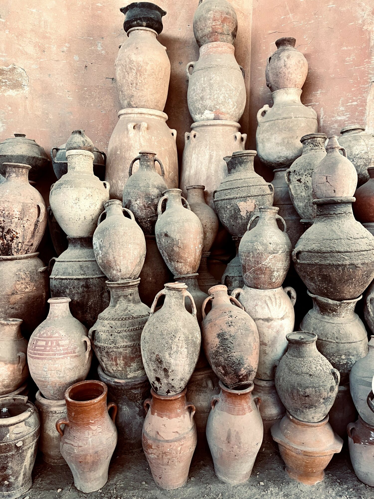 Collection of ancient clay pots and jars stacked against a wall, varying in size and shape, some with handles.
