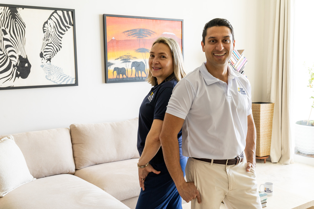 Two people standing in a living room with artwork on the wall, smiling and holding hands.