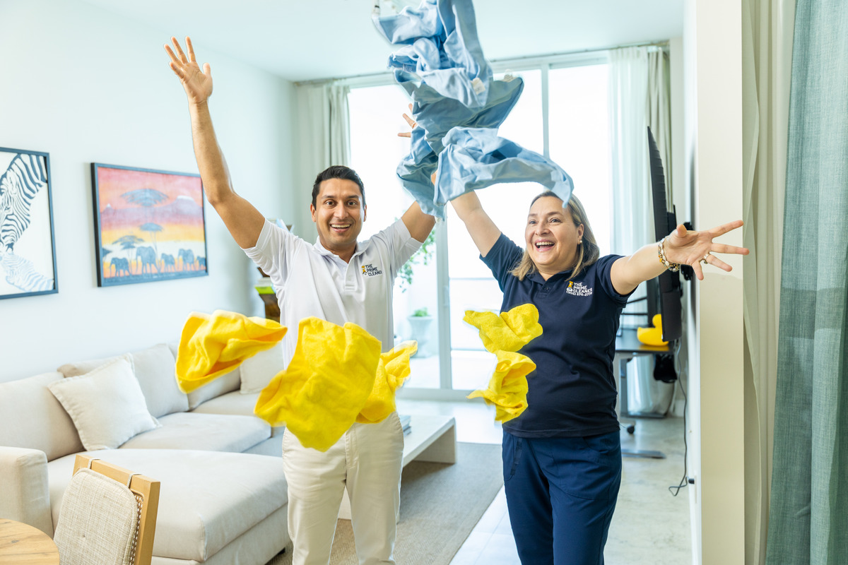 Two people celebrating indoors with yellow paper decorations, smiling and making peace signs, in a bright living room.