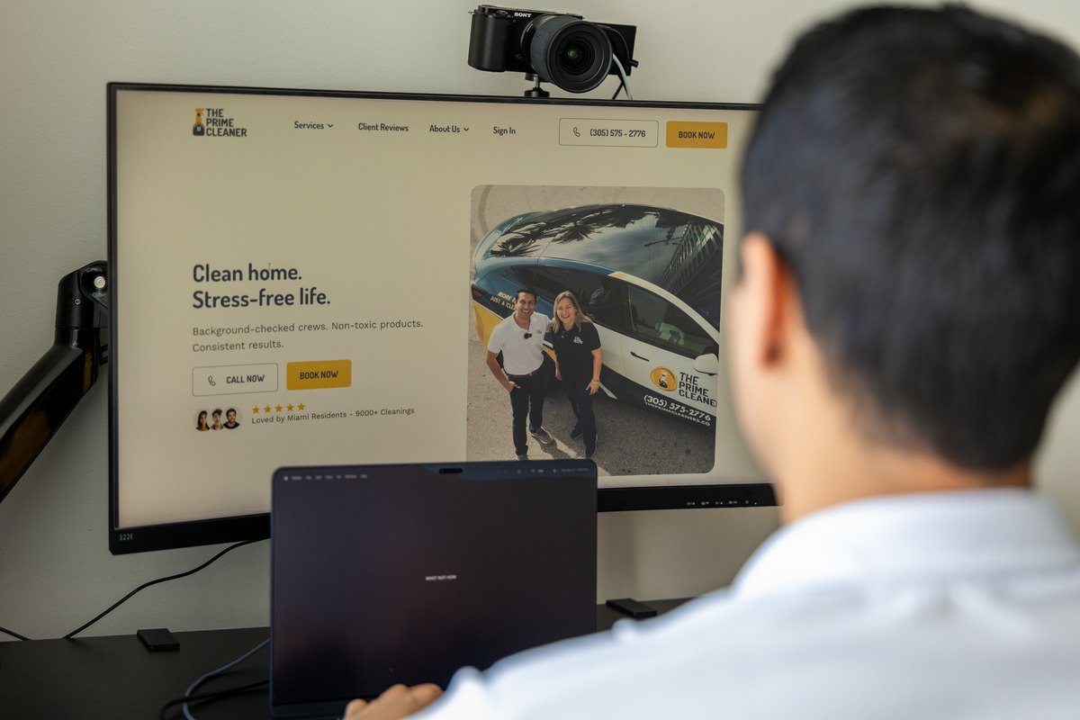 Person with dark hair and white shirt watching a computer screen displaying a website with a photo of two people and a vehicle.