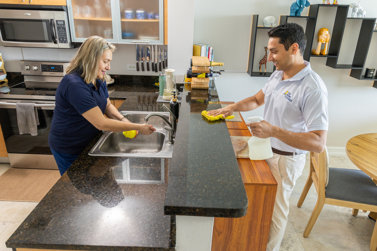 Two people in a kitchen, one washing dishes at the sink, the other preparing food at the counter.