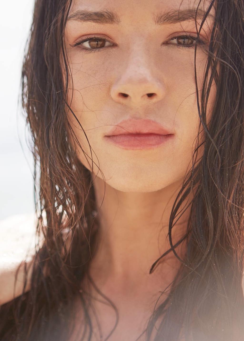 Close-up of a woman with wet hair and a neutral expression, outdoors with bright lighting.
