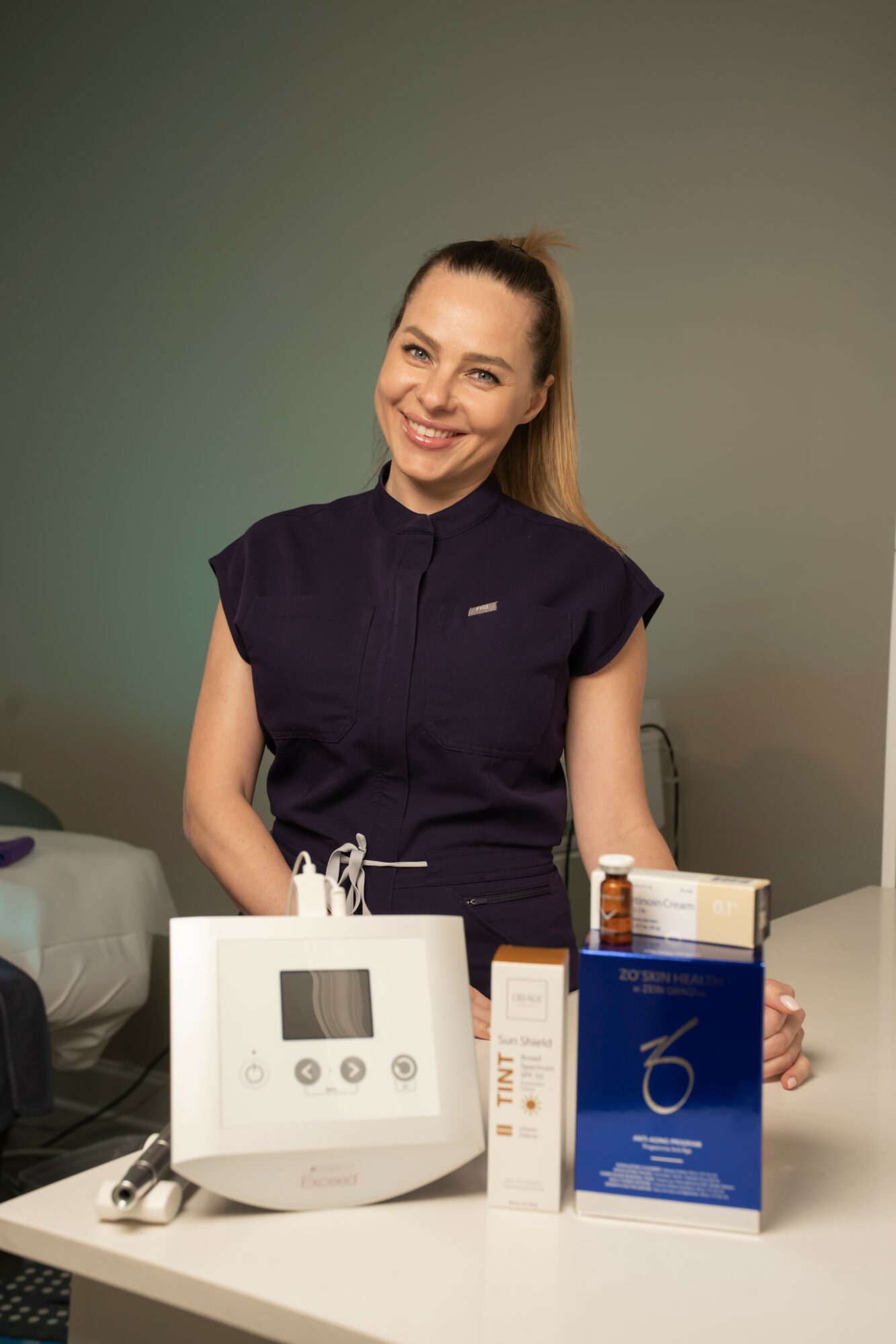 Smiling woman in dark uniform standing behind a medical device on a table.