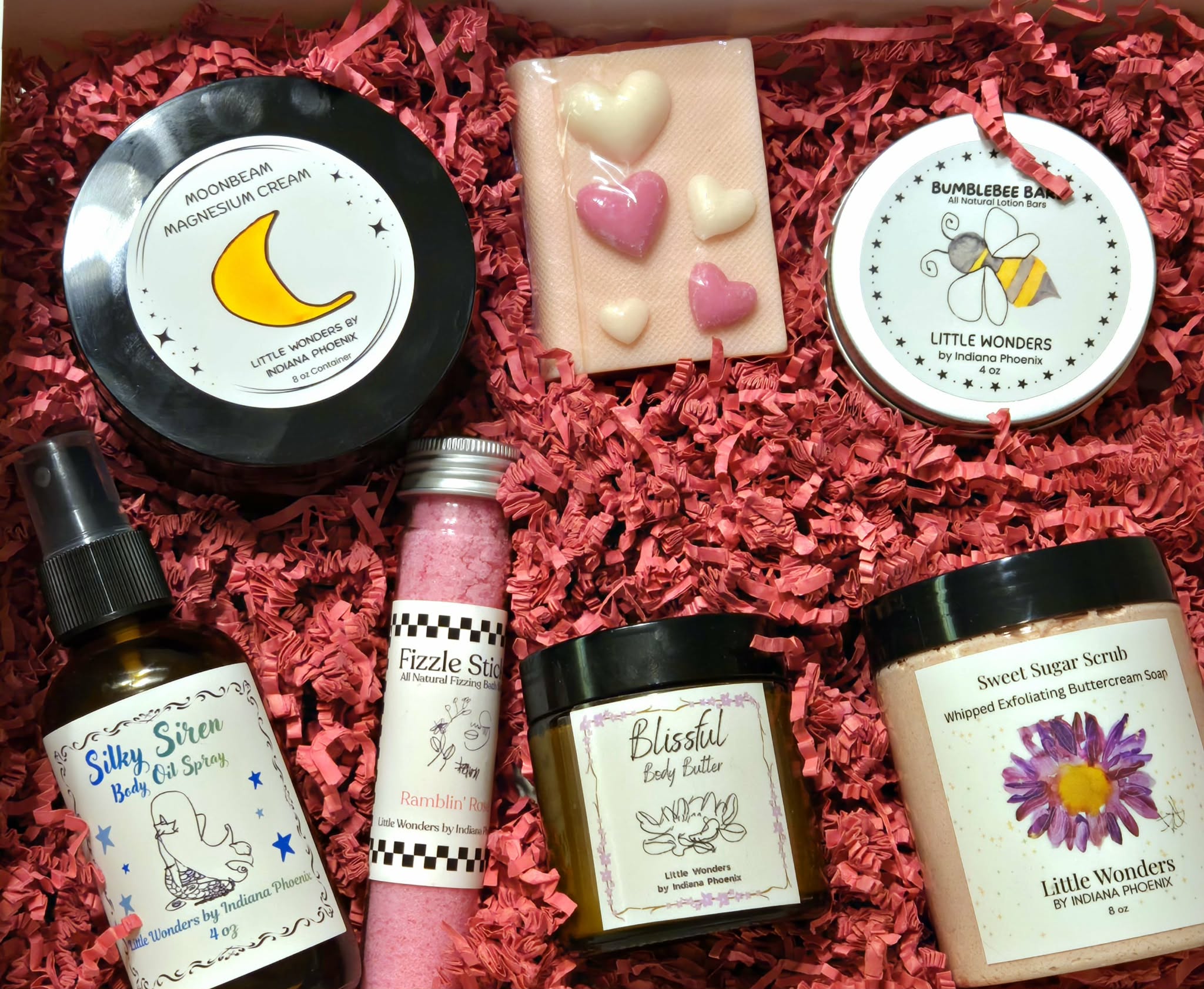 Assorted skincare and cosmetic products on red shredded paper, including creams, sprays, and a soap bar with pink and white hearts.