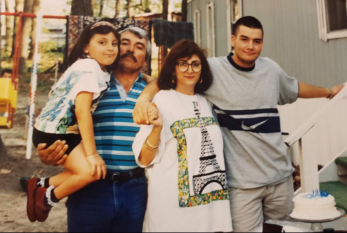 Four people standing outdoors, two adults and two children, smiling and posing for the photo.