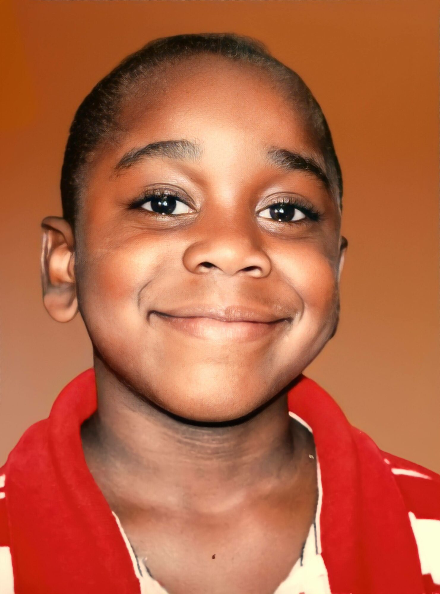 Young girl with a smile, wearing a red hoodie, against a warm brown background.