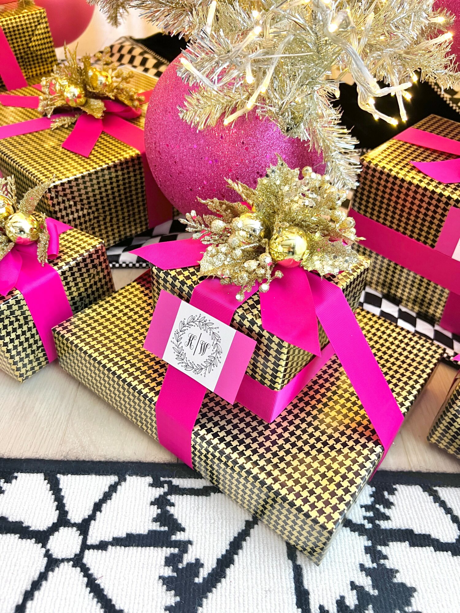 Wrapped Christmas presents with pink ribbons, a pink ornament, and gold decorations on a patterned rug.