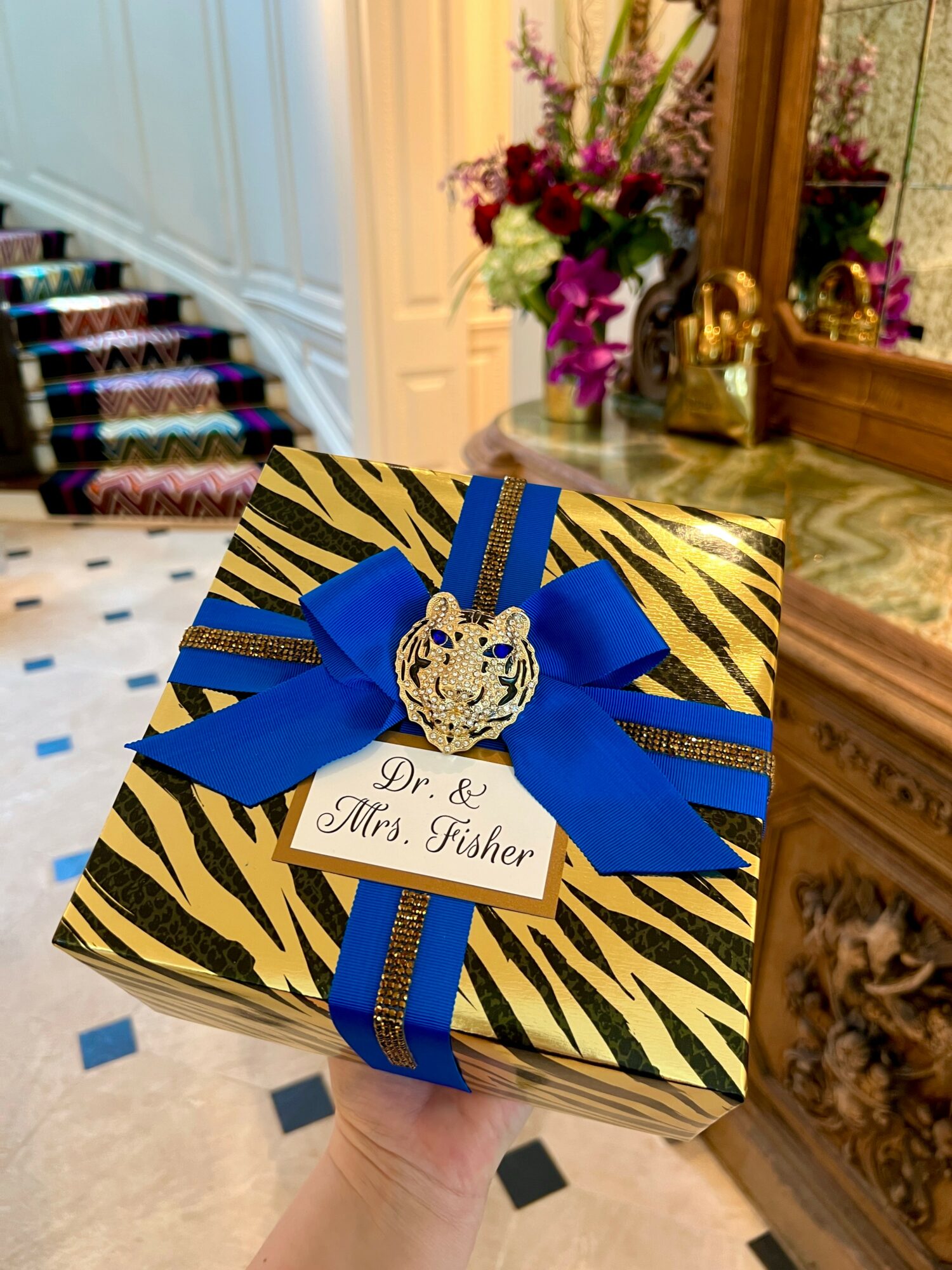 Decorative gift box with blue ribbon, gold tiger emblem, and a tag reading 'Dr. & Mrs.. Fisher'.