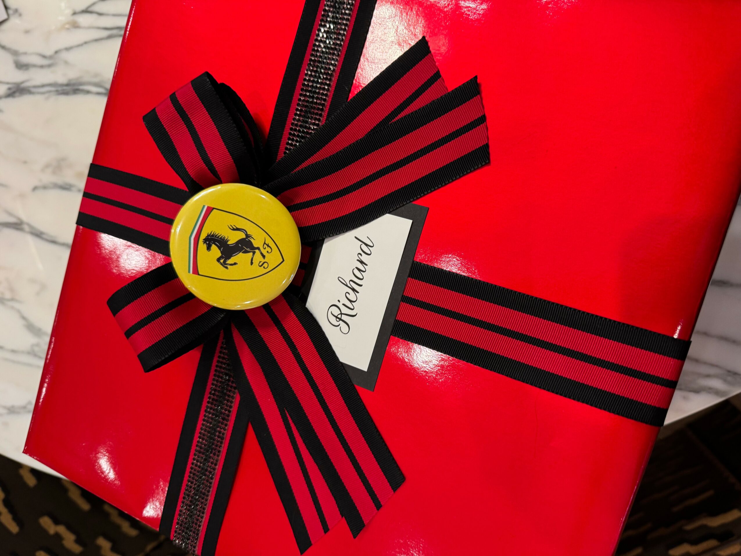 Red gift box with black striped ribbon, yellow button with a black horse, and a white tag reading 'Stefanie'.